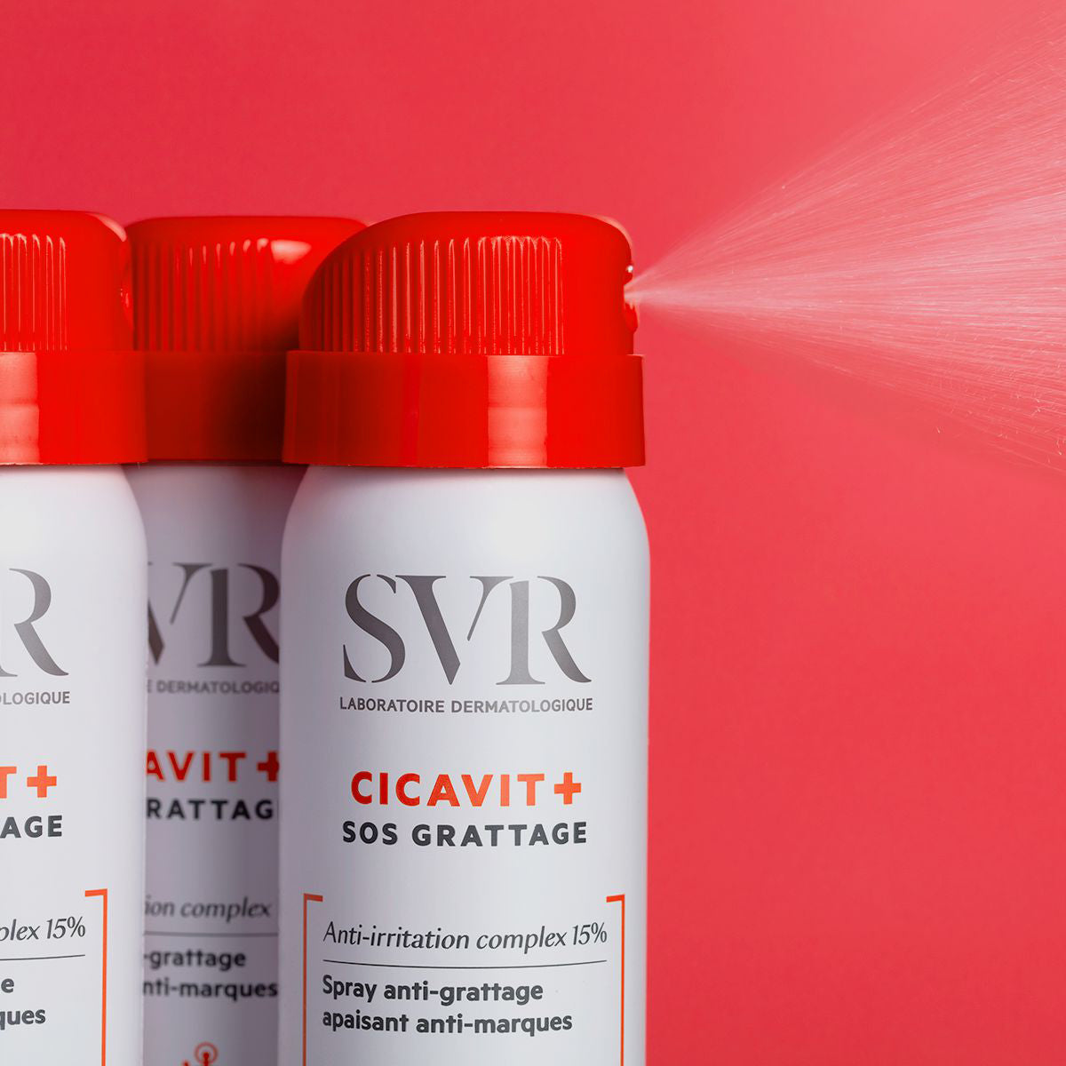 Spray SVR Cicavit+ SOS Grattage en envase blanco con tapón rojo pulverizando una fina bruma sobre fondo rojo.
