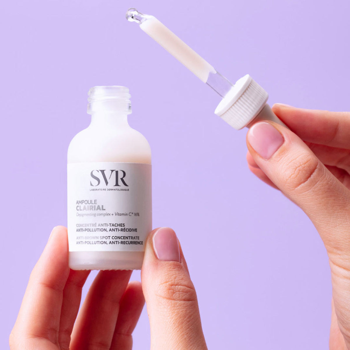 Frasco de vidrio esmerilado SVR Clairial Ampoule con gotero, sostenido por manos sobre fondo lila.