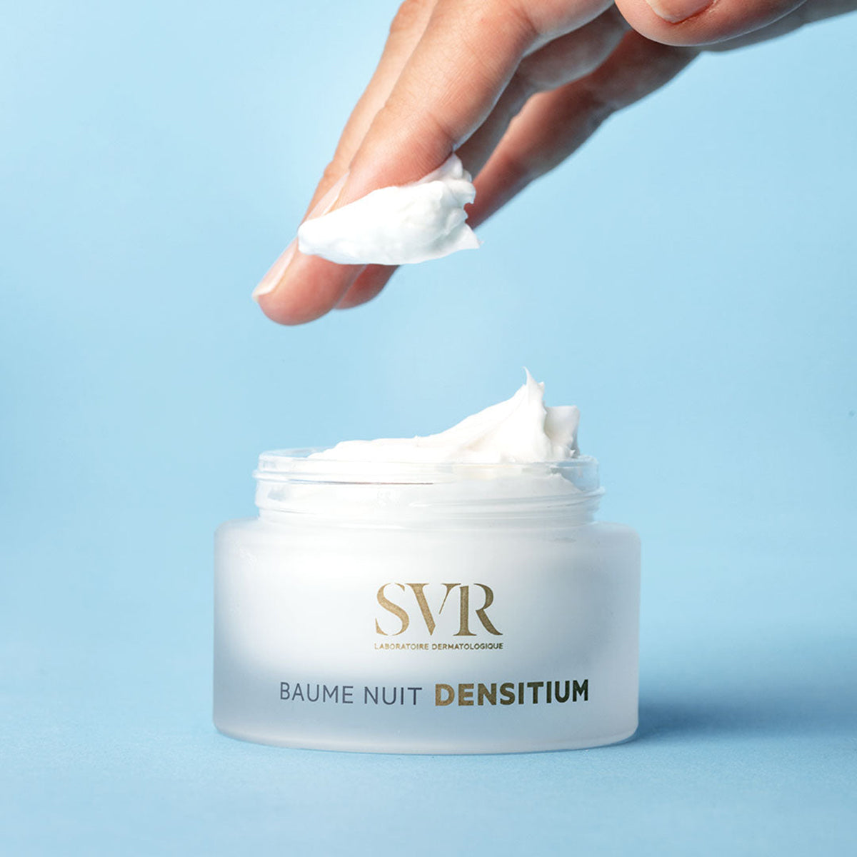 SVR Densitium Baume Nuit night cream in a frosted glass jar with a finger holding a dollop of rich white cream.