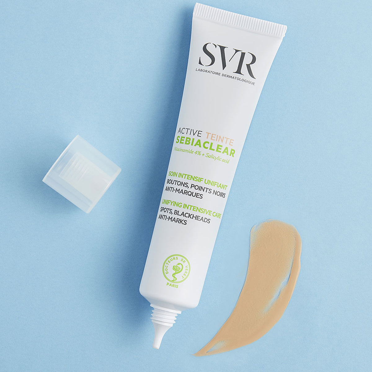 Tubo blanco de SVR Sebiaclear Active Teinté con tapa abierta y una muestra de textura fluida color beige sobre fondo azul.