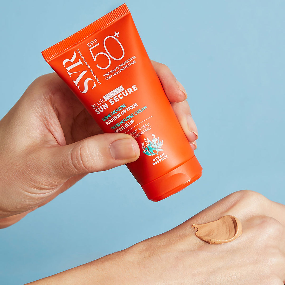 Tubo naranja de protector solar SVR Sun Secure Blur Teinte con textura mousse aplicada sobre el dorso de la mano.