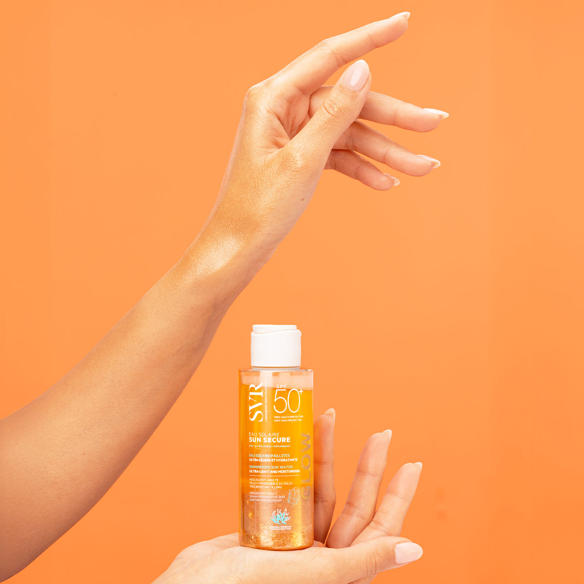SVR SUN SECURE SPF50+ shimmering sun water bottle held by a hand with glowing, golden-toned skin against an orange background.