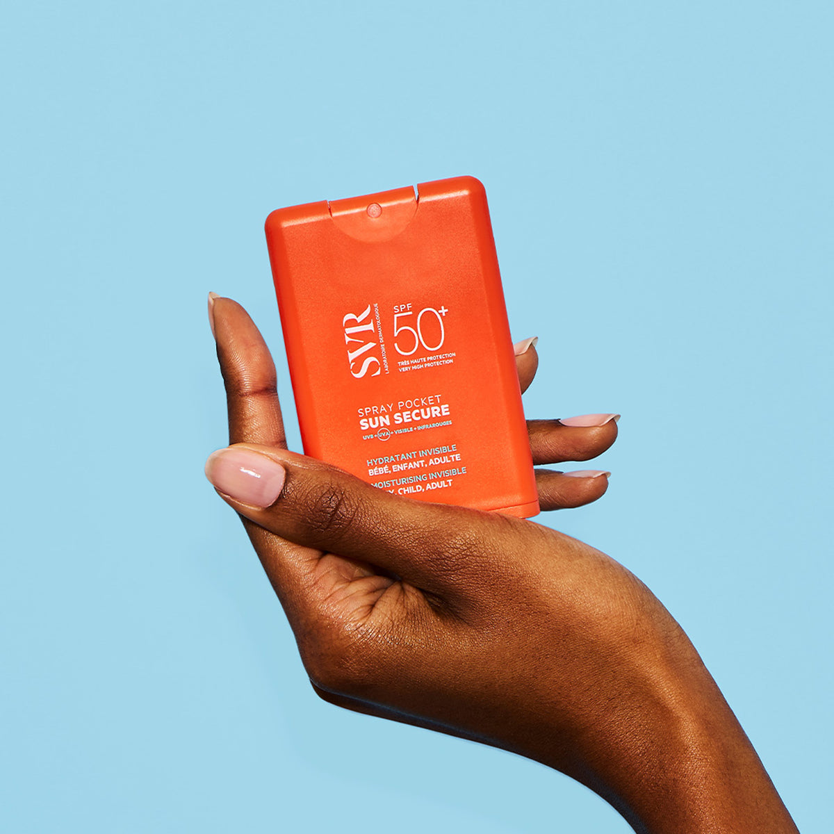 Mano sosteniendo un envase naranja compacto de protector solar SVR Sun Secure Spray Pocket SPF50+ sobre fondo azul claro.