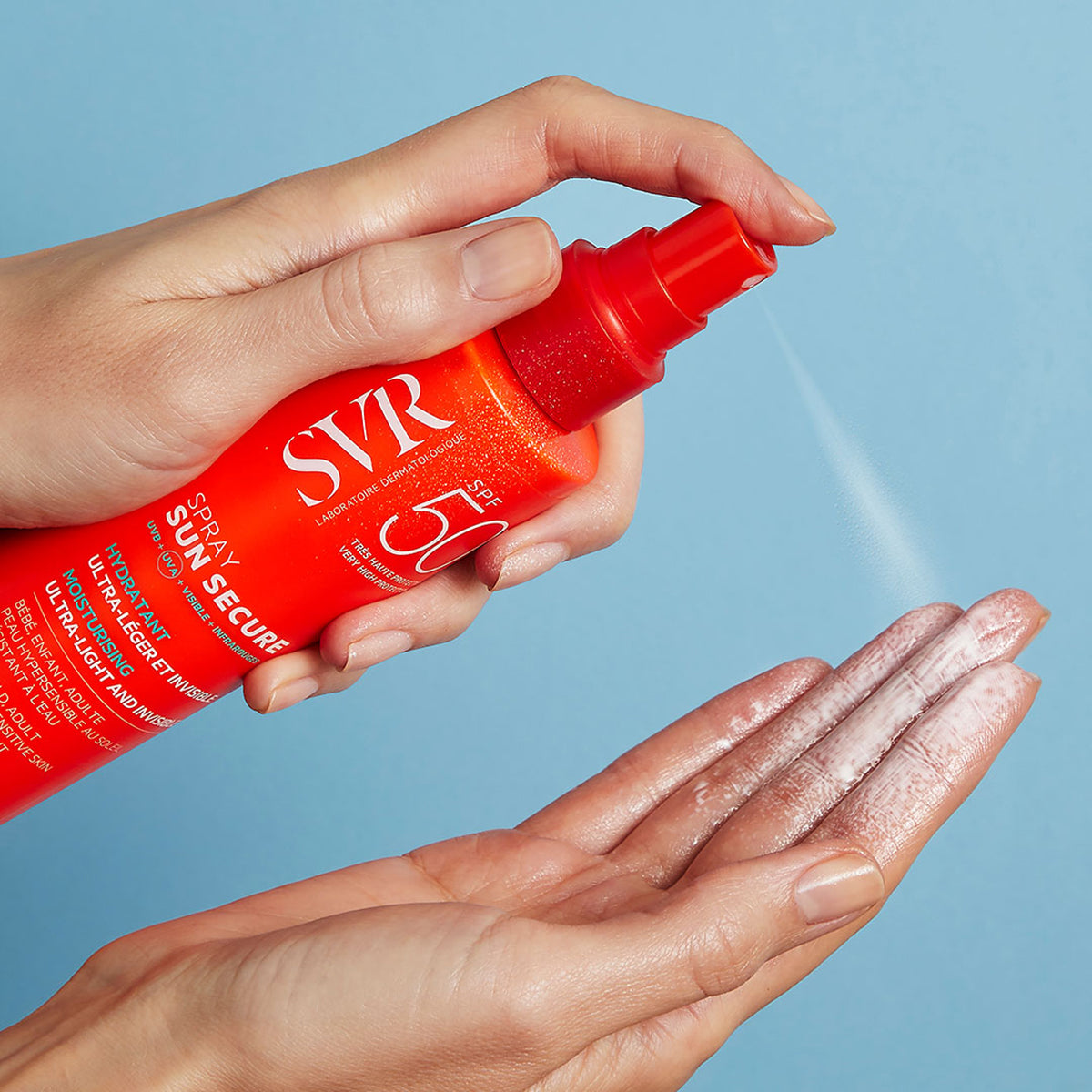Mano aplicando protector solar SVR Sun Secure Spray SPF50+ de envase naranja sobre la palma de la mano con fondo azul.