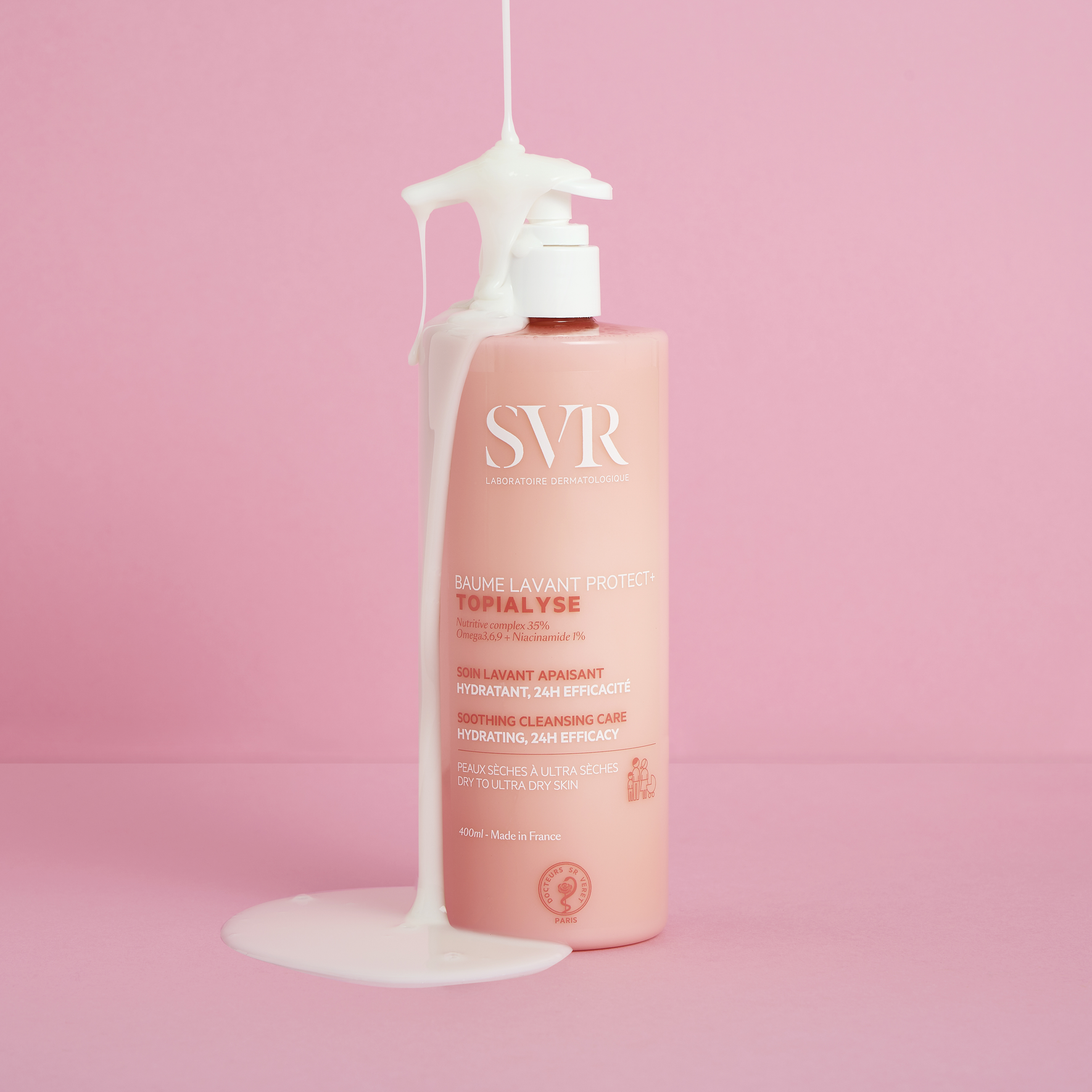 Frasco rosa de 400ml de SVR Topialyse Baume Lavant con textura cremosa cayendo sobre fondo rosa pastel.