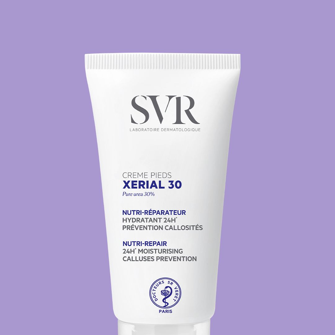 Tubo blanco de crema SVR XERIAL 30 para pies sobre fondo lila, con texto azul y negro detallando sus beneficios hidratantes.