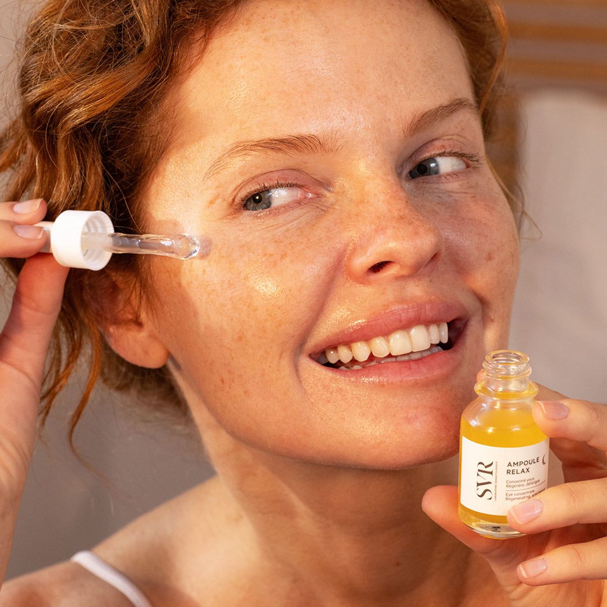 Mujer aplicando sérum SVR Ampoule Relax con pipeta sobre el contorno de ojos, frasco de vidrio amarillo en mano.