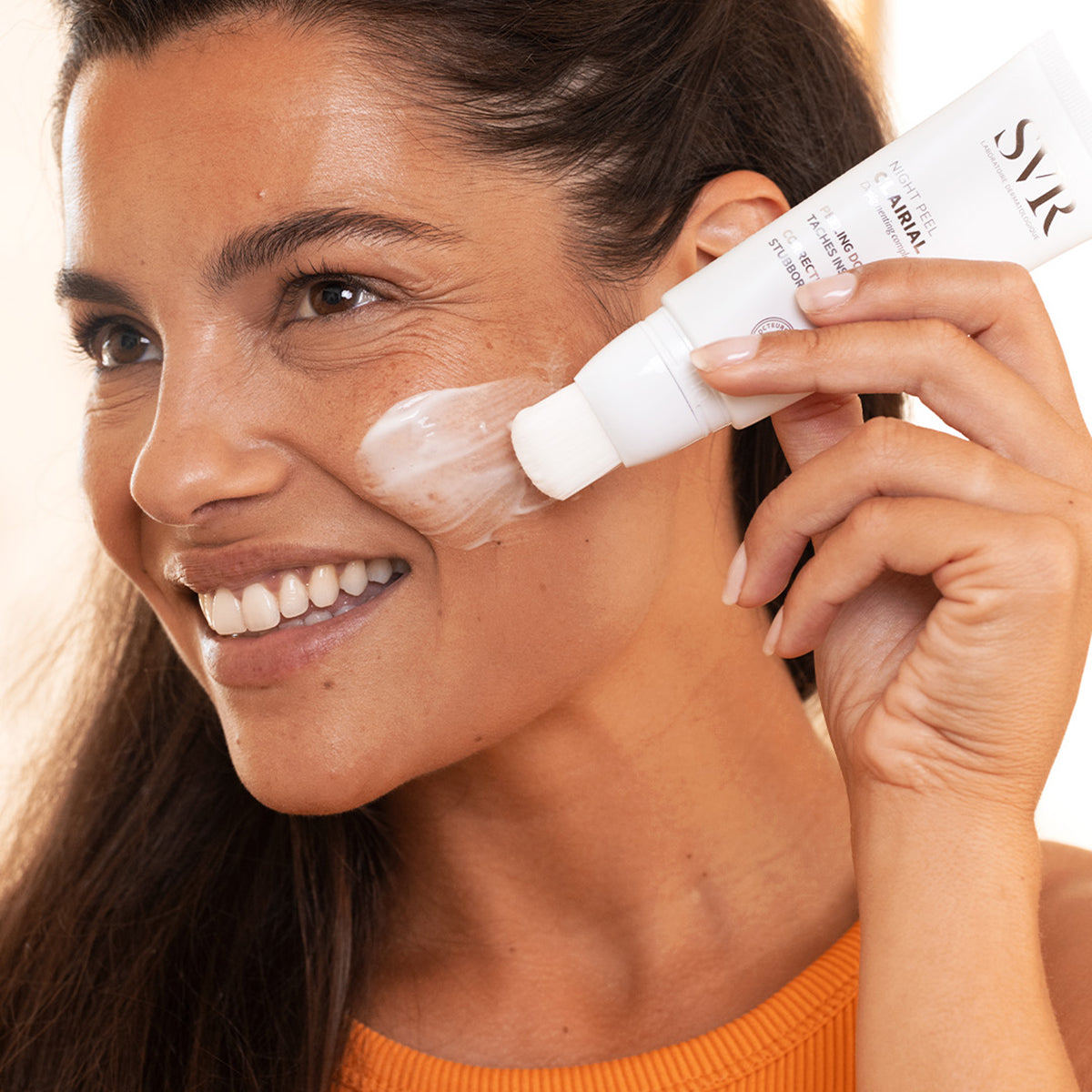 Mujer aplicándose SVR Clairial Night Peel con aplicador de pincel sobre la mejilla para tratar manchas oscuras.