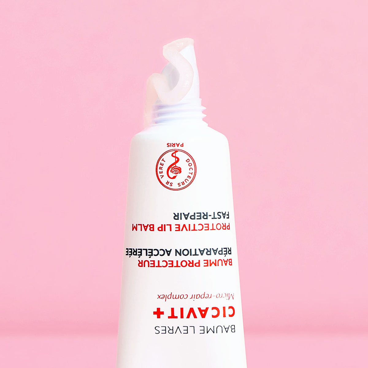 Tubo blanco de bálsamo reparador Cicavit+ Lèvres con textura transparente sobre fondo rosa suave.