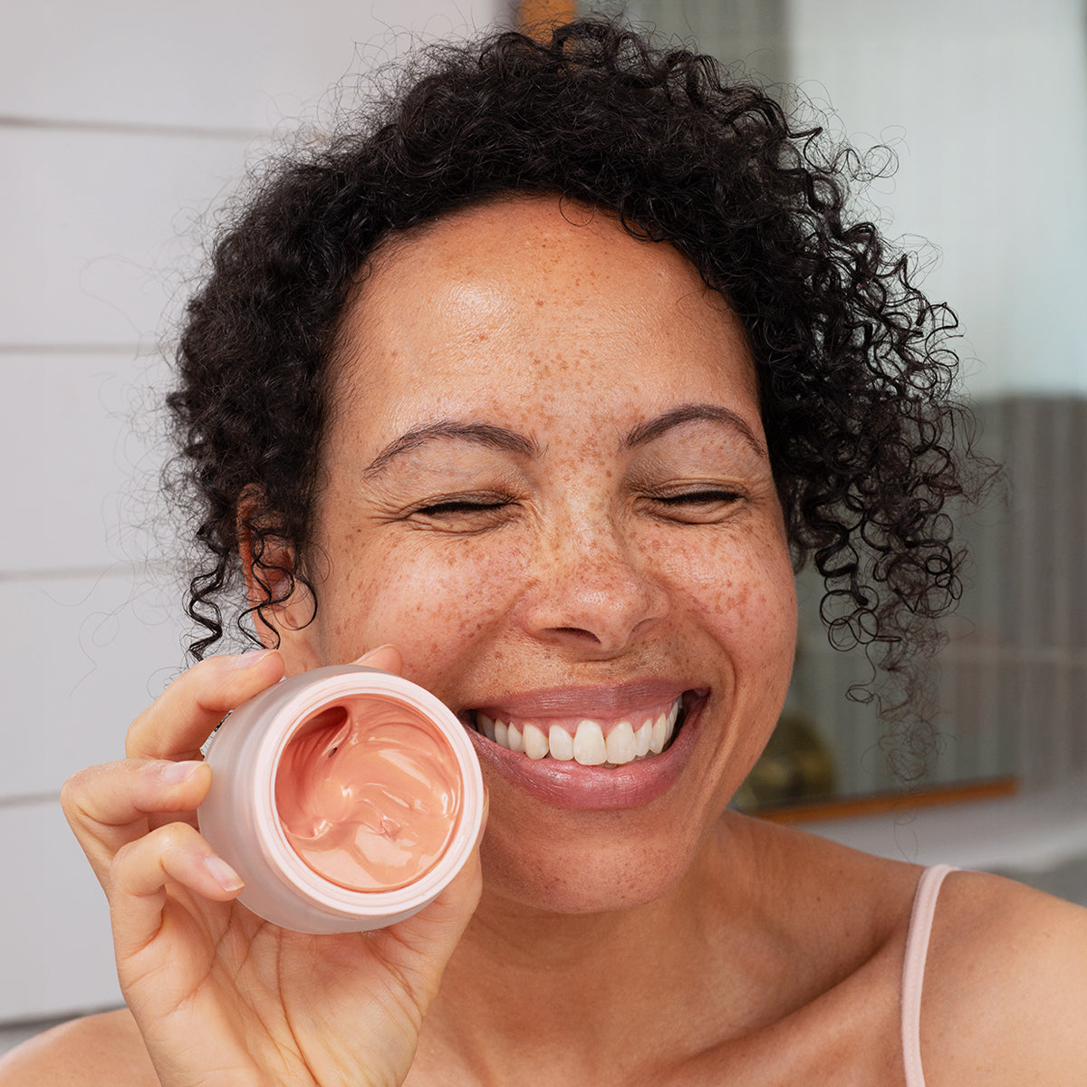 Mujer sonriente sosteniendo un tarro de crema facial rosada DENSITIUM Rose Eclat con textura sedosa y acabado luminoso.