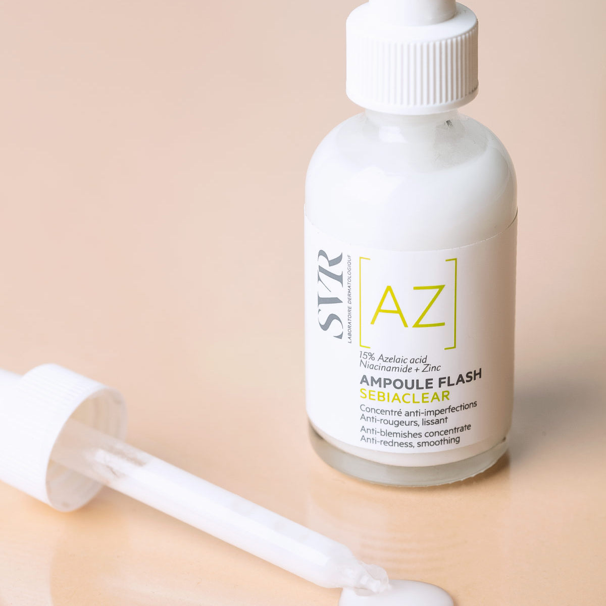 Frasco de vidrio SVR Sebiaclear Ampoule Flash con gotero y suero lechoso sobre fondo beige suave.
