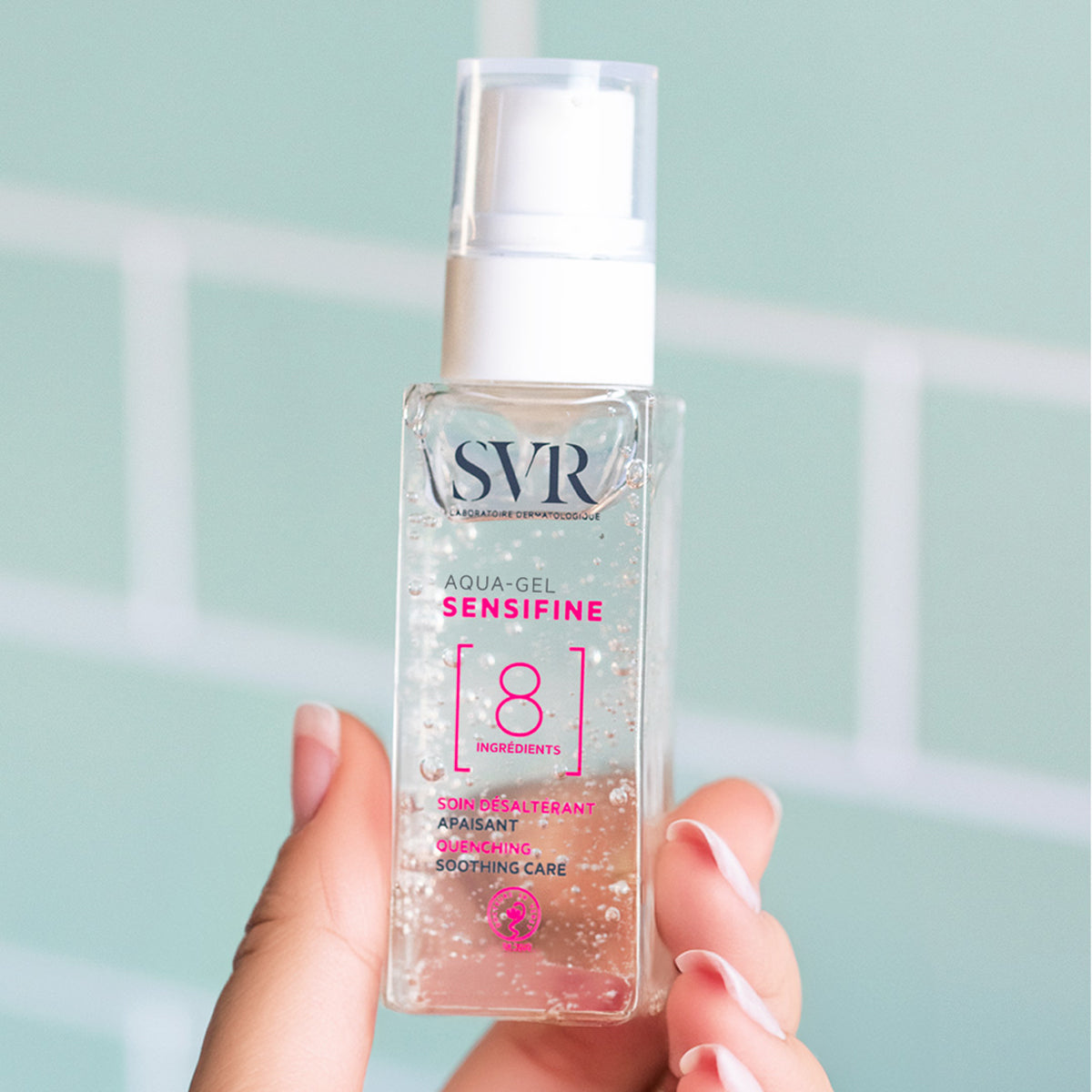Frasco transparente de gel hidratante SVR Sensifine con dosificador blanco, sostenido en la mano sobre fondo azul claro.