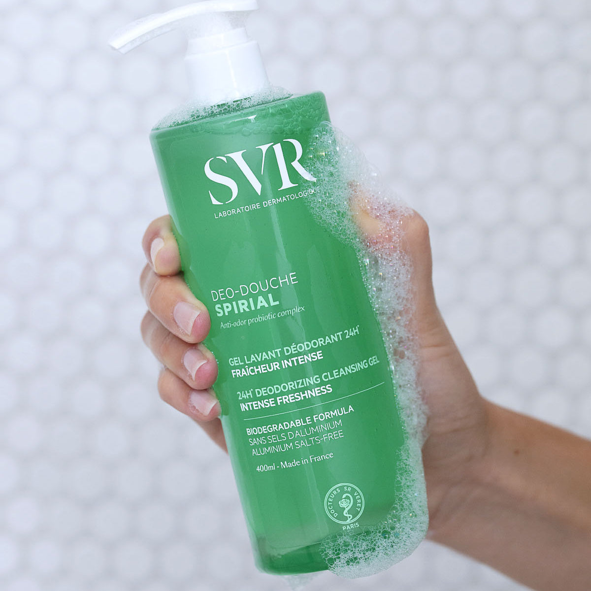 Envase verde de gel de ducha SVR Spirial de 400ml con dosificador, sostenido en una mano con espuma limpiadora.