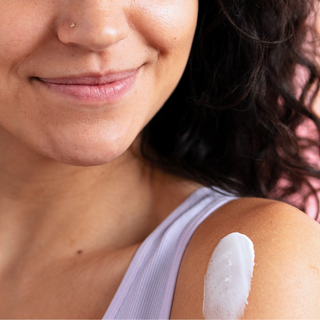 Mujer sonriente aplicando una crema blanca nutritiva TOPIALYSE sobre su hombro para hidratar la piel.