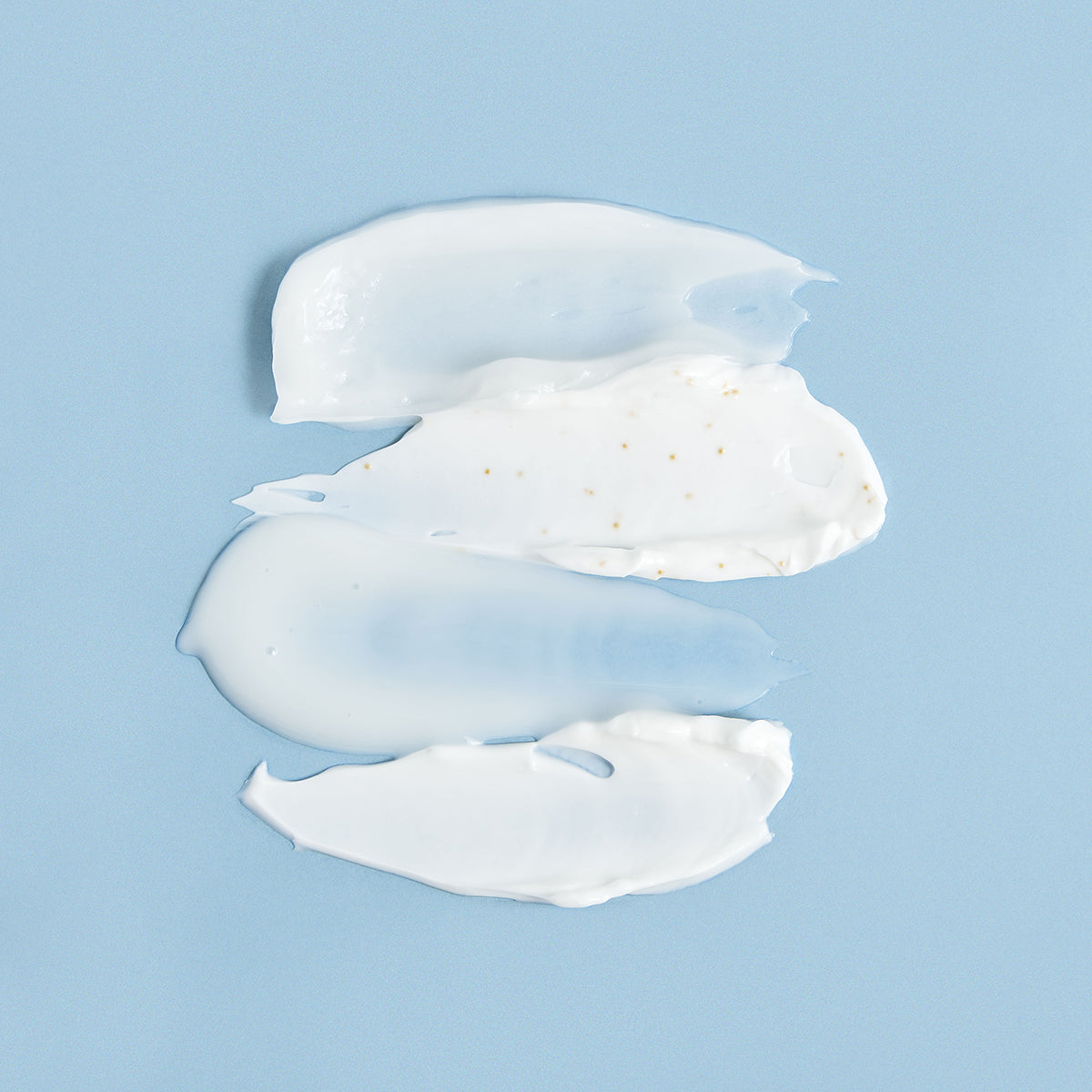 Muestras de crema blanca con textura suave y partículas sobre un fondo azul claro.