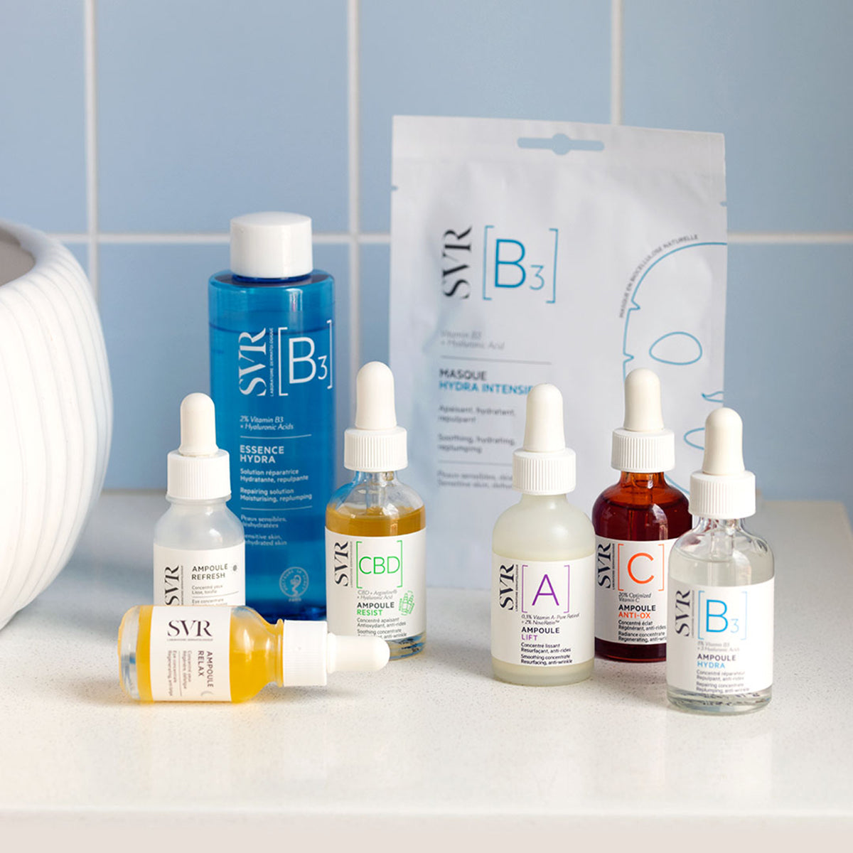Sérum SVR Ampoule Anti-Ox en frasco de vidrio ámbar con gotero junto a otros productos de la línea SVR sobre una mesa blanca.
