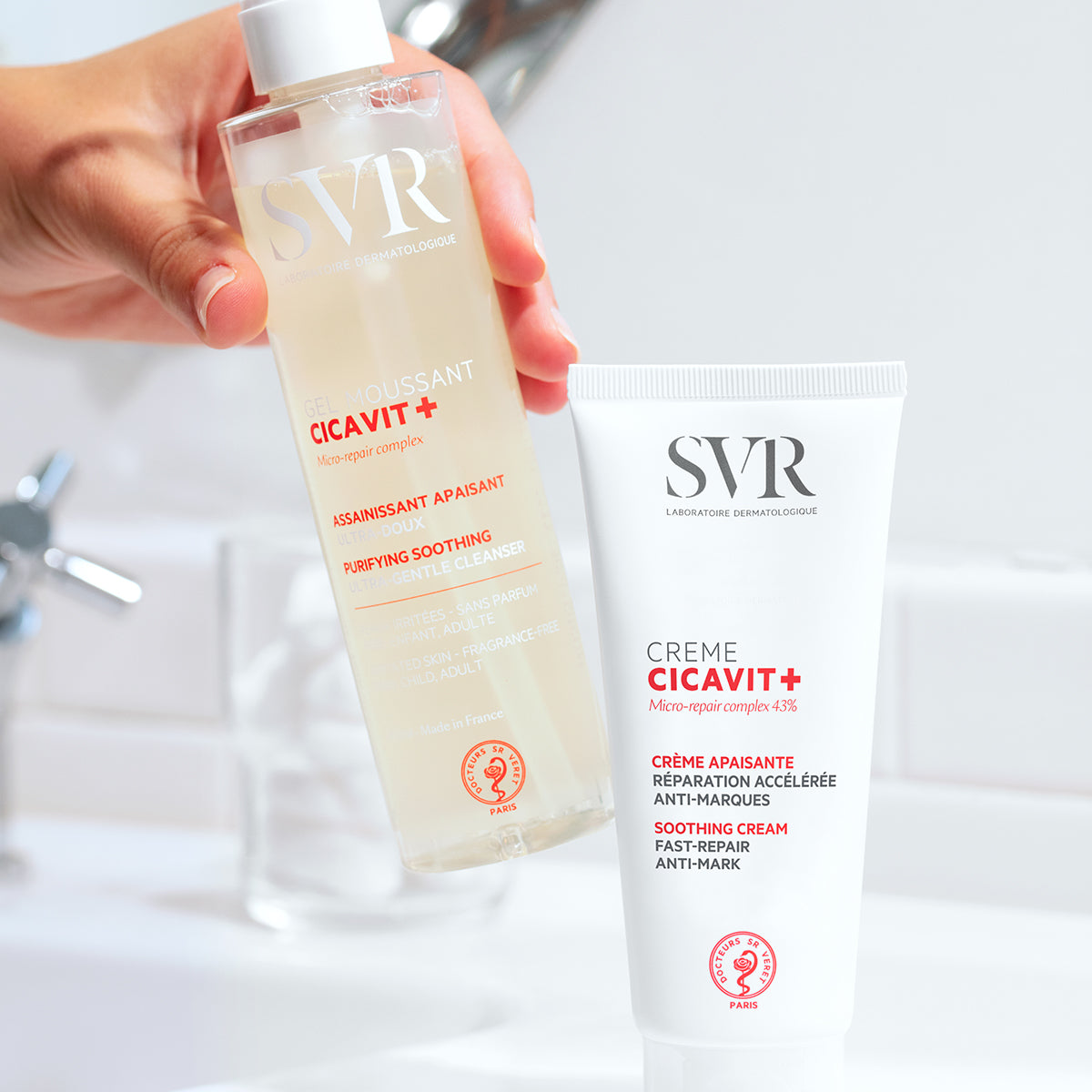 Botella transparente de gel limpiador SVR Cicavit+ y tubo de crema reparadora blanca sobre fondo de baño.