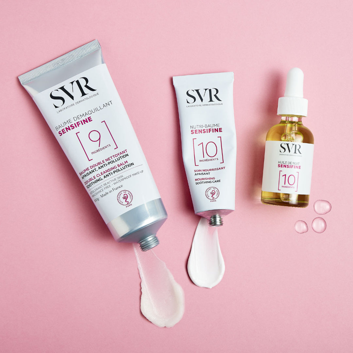 Set de productos SVR Sensifine con bálsamo limpiador, crema nutritiva y aceite facial sobre fondo rosa.