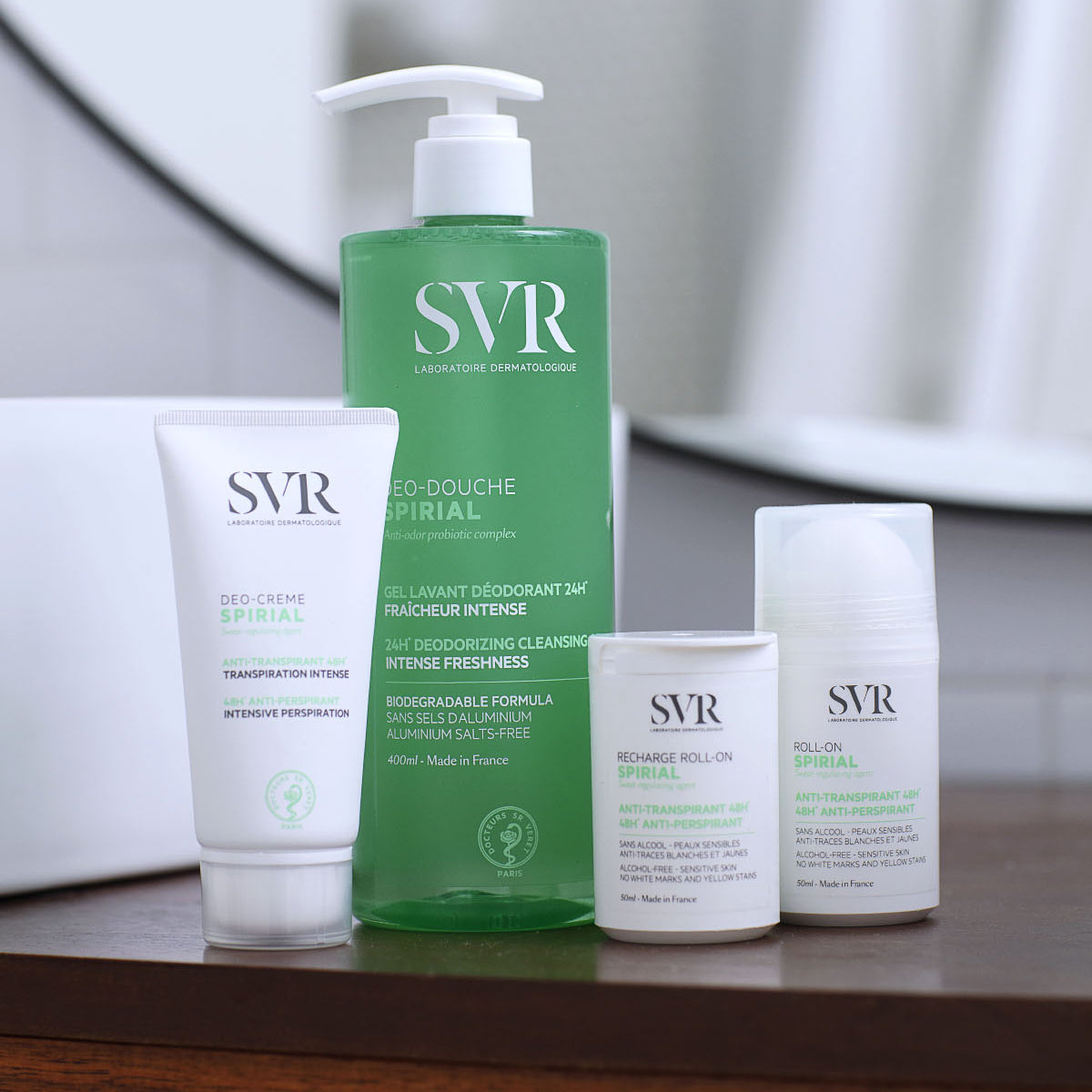 SVR Spirial desodorante en crema, gel de ducha y roll-on sobre una superficie de madera, diseño minimalista en blanco y verde.