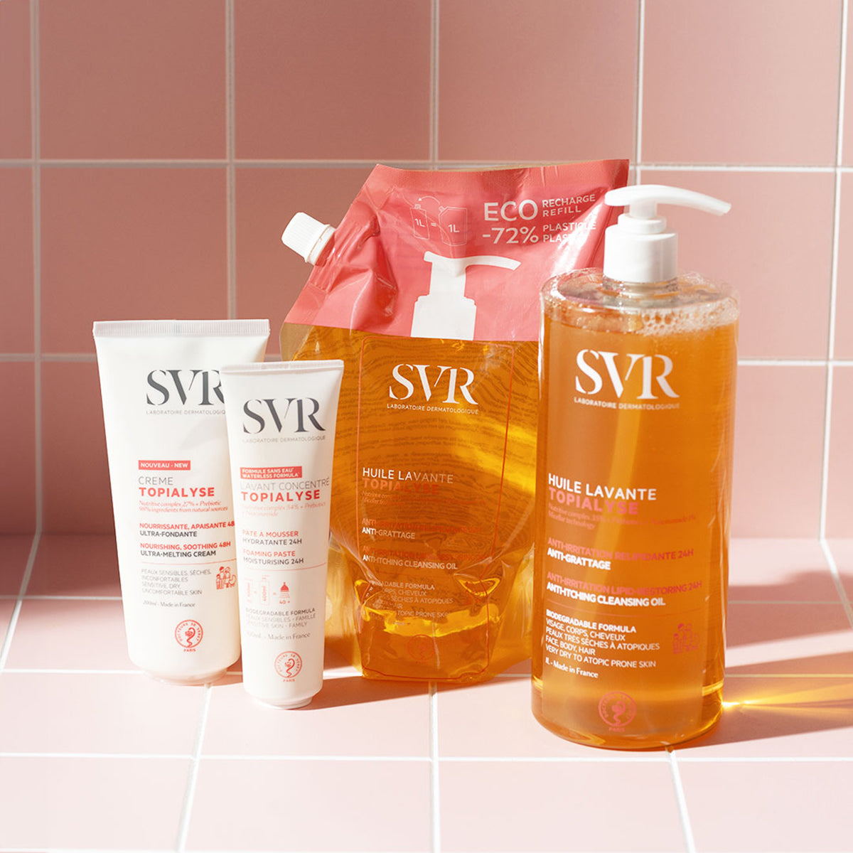 SVR Topialyse skincare collection including tubes, an eco-refill pouch, and a pump bottle on a pink tiled background.