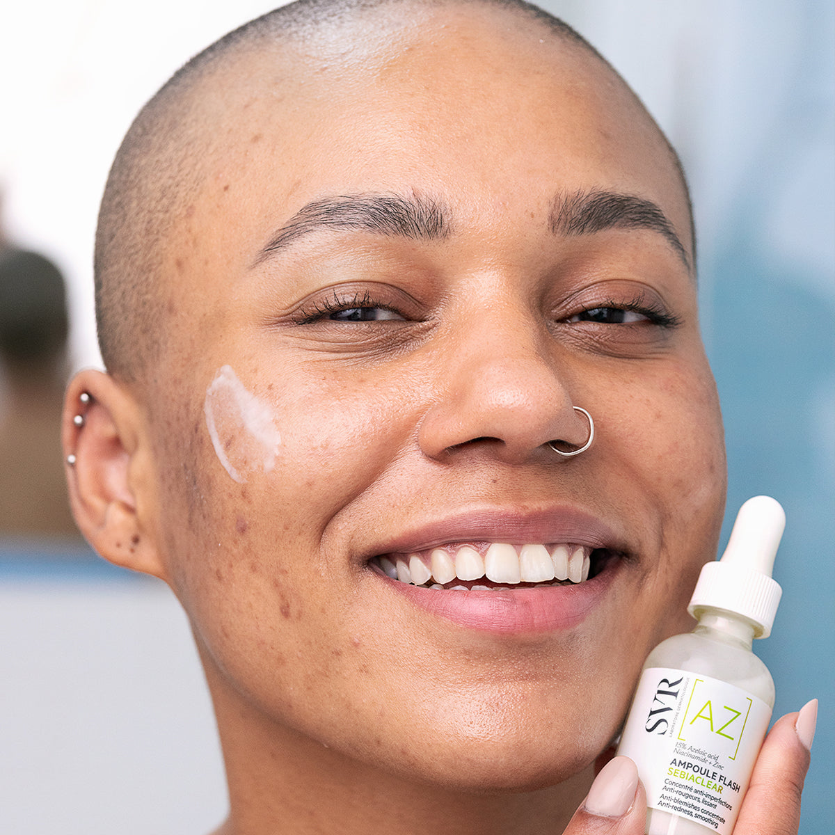 Persona sonriente con SEBIACLEAR Ampoule Flash, un frasco de vidrio con gotero y etiqueta blanca y verde para pieles con acné.