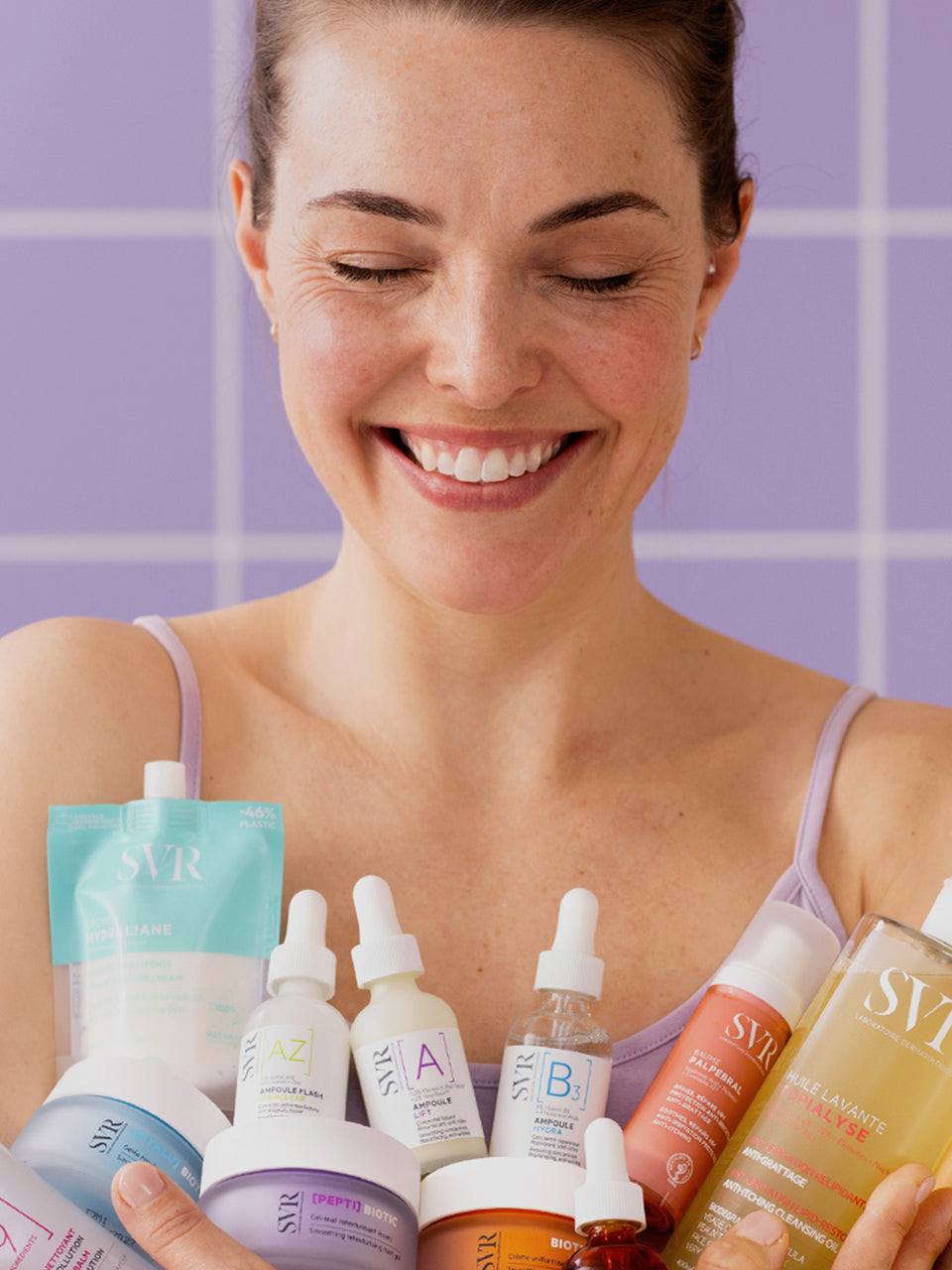 Mujer sonriendo con productos dermocosméticos de SVR en las manos, ilustrando una rutina de cuidado de la piel.