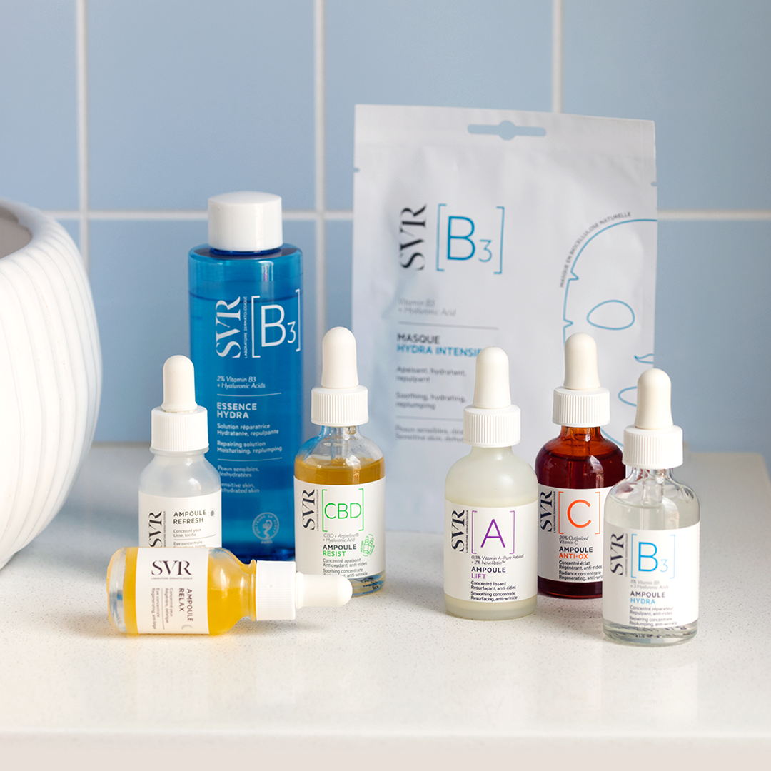 Colección de sérums SVR Ampoule con frascos de vidrio, goteros y mascarilla facial B3 sobre una superficie blanca.