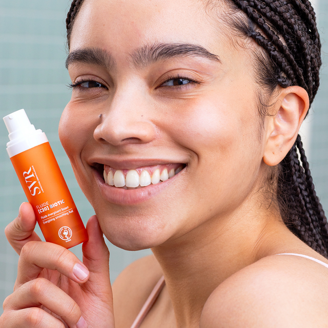 Mujer con piel luminosa sosteniendo el fluido antioxidante SVR [C20] Biotic, tratamiento facial con vitamina C para revitalizar y alisar la piel.