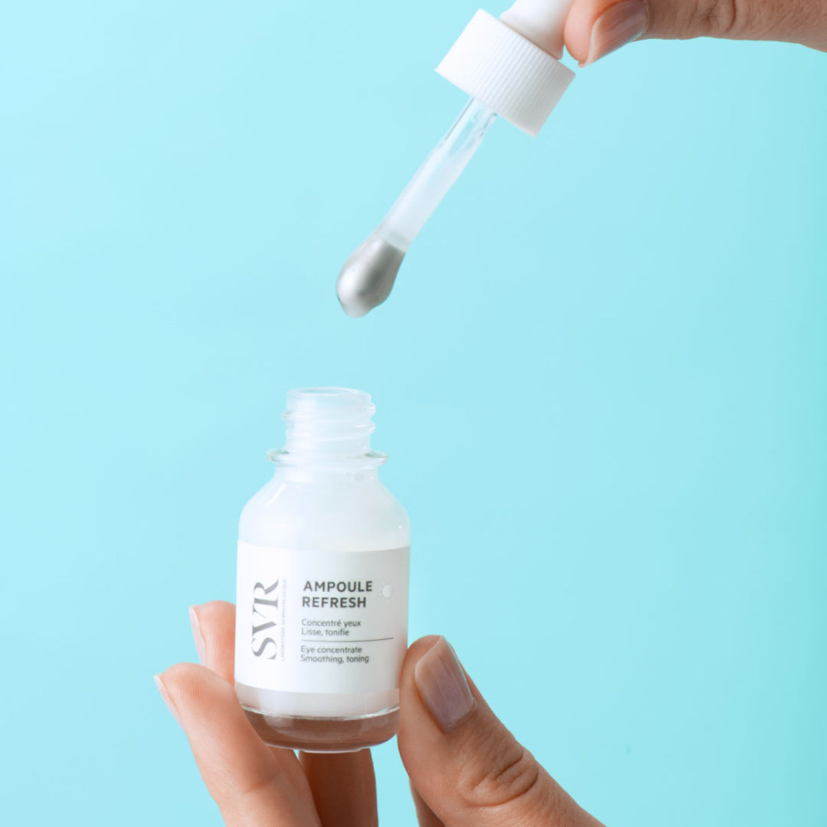 Frasco de SVR Ampoule Refresh con aplicador de pipeta metálica para el contorno de ojos sobre fondo azul claro.