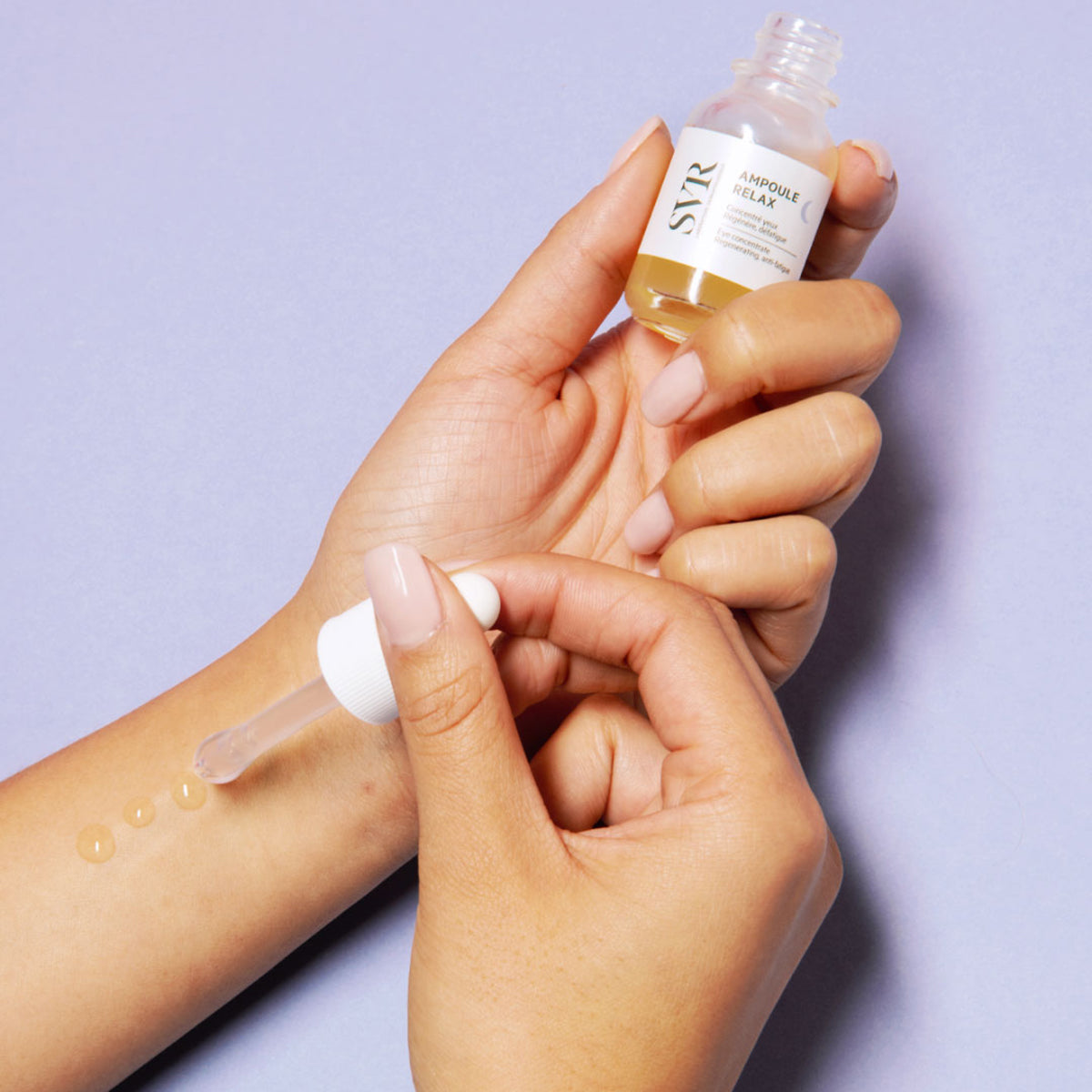 Sérum SVR Ampoule Relax en frasco de cristal con pipeta aplicadora sobre fondo lila, aplicando gotas doradas en la muñeca.