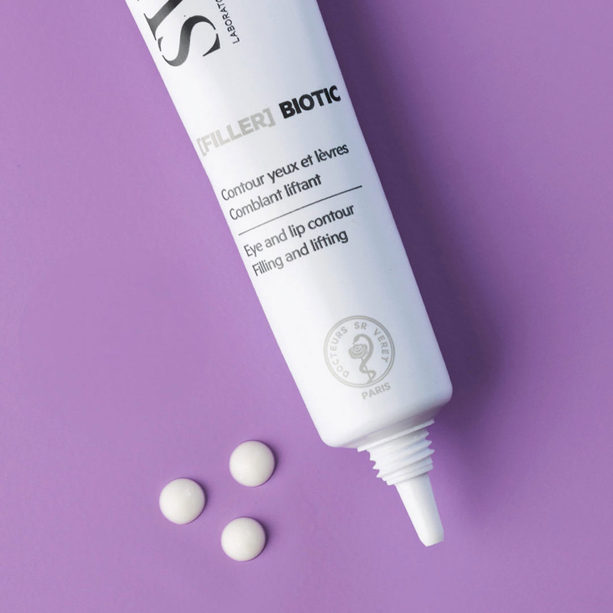 Tubo blanco de crema [FILLER] Biotic para ojos y labios con tres gotas de producto sobre un fondo morado liso.
