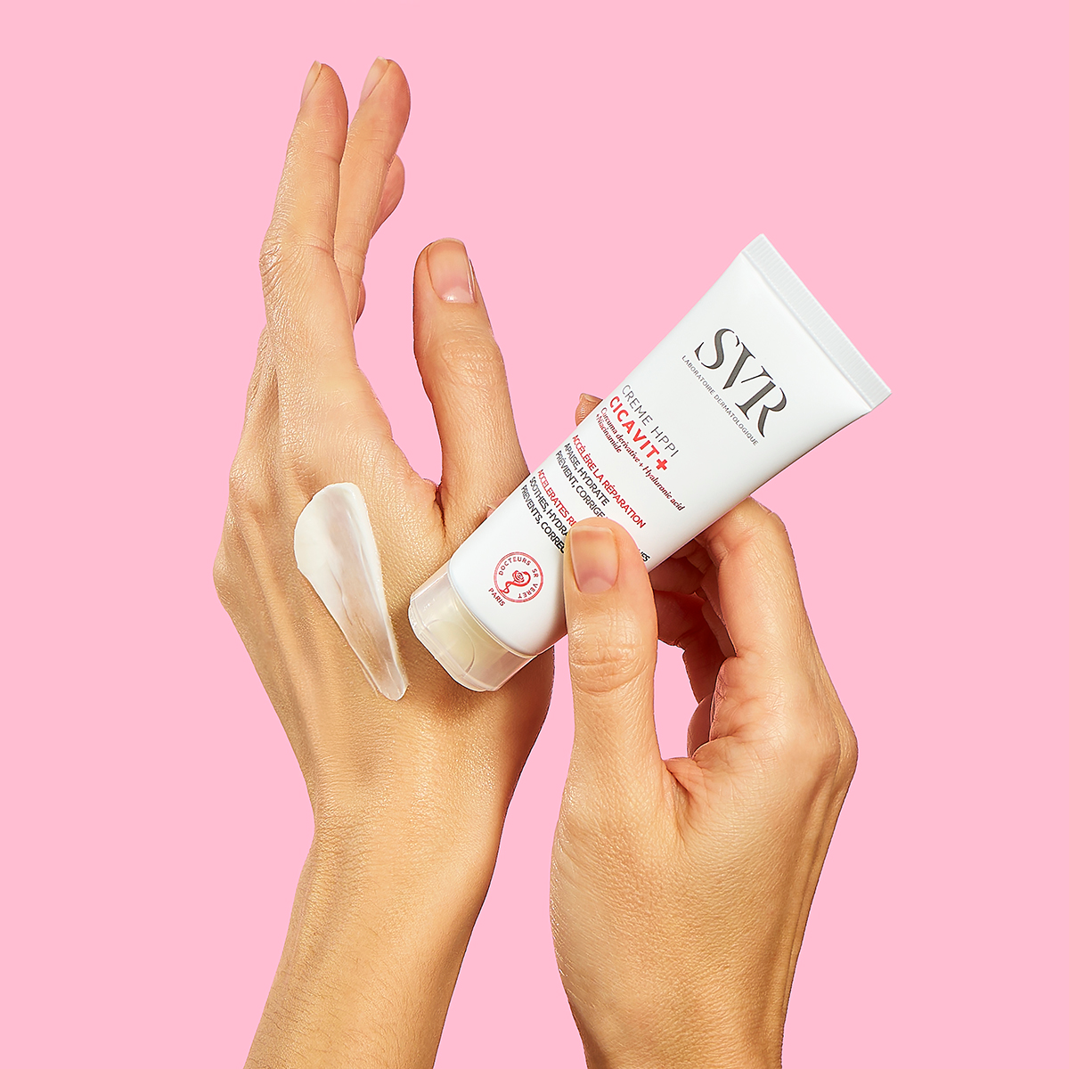 Tubo blanco de crema SVR Cicavit+ HPPI aplicado sobre la mano, mostrando su textura reparadora sobre fondo rosa.