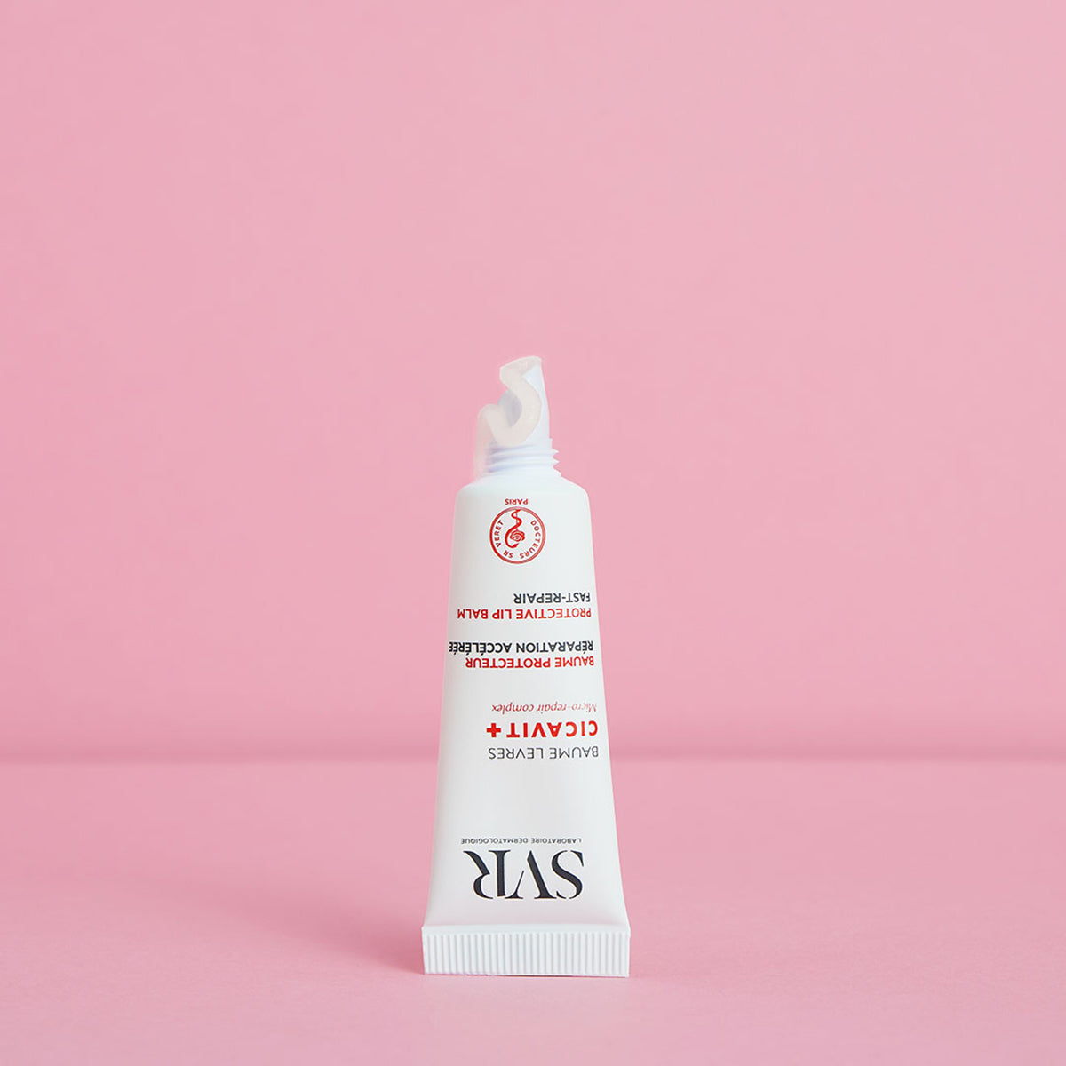 Tubo blanco de bálsamo labial reparador SVR Cicavit+ con textura transparente sobre fondo rosa pastel.