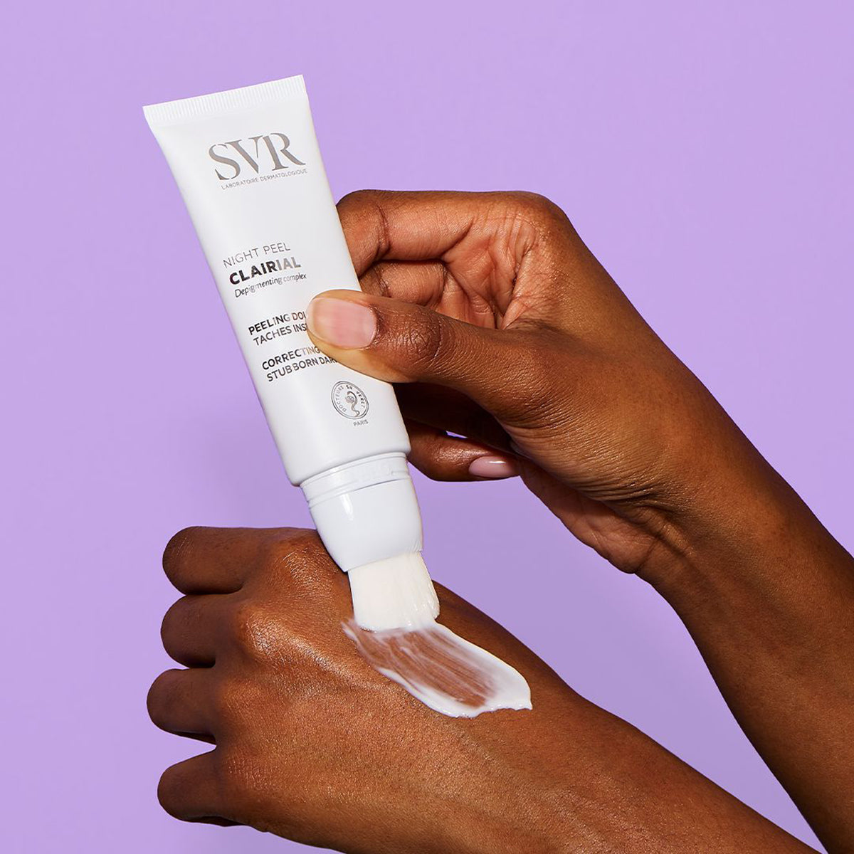 Tubo blanco de SVR Clairial Night Peel aplicando crema con su pincel integrado sobre el dorso de una mano.