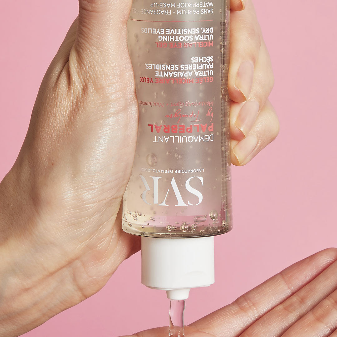 Frasco transparente de gel desmaquillante SVR Palpebral siendo aplicado sobre una mano con fondo rosa suave.