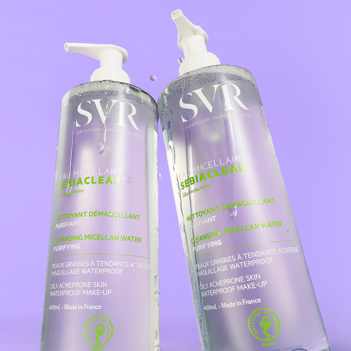 Dos frascos de 400ml de agua micelar SVR Sebiaclear con dosificador sobre fondo lila, mostrando gotas de agua purificante.