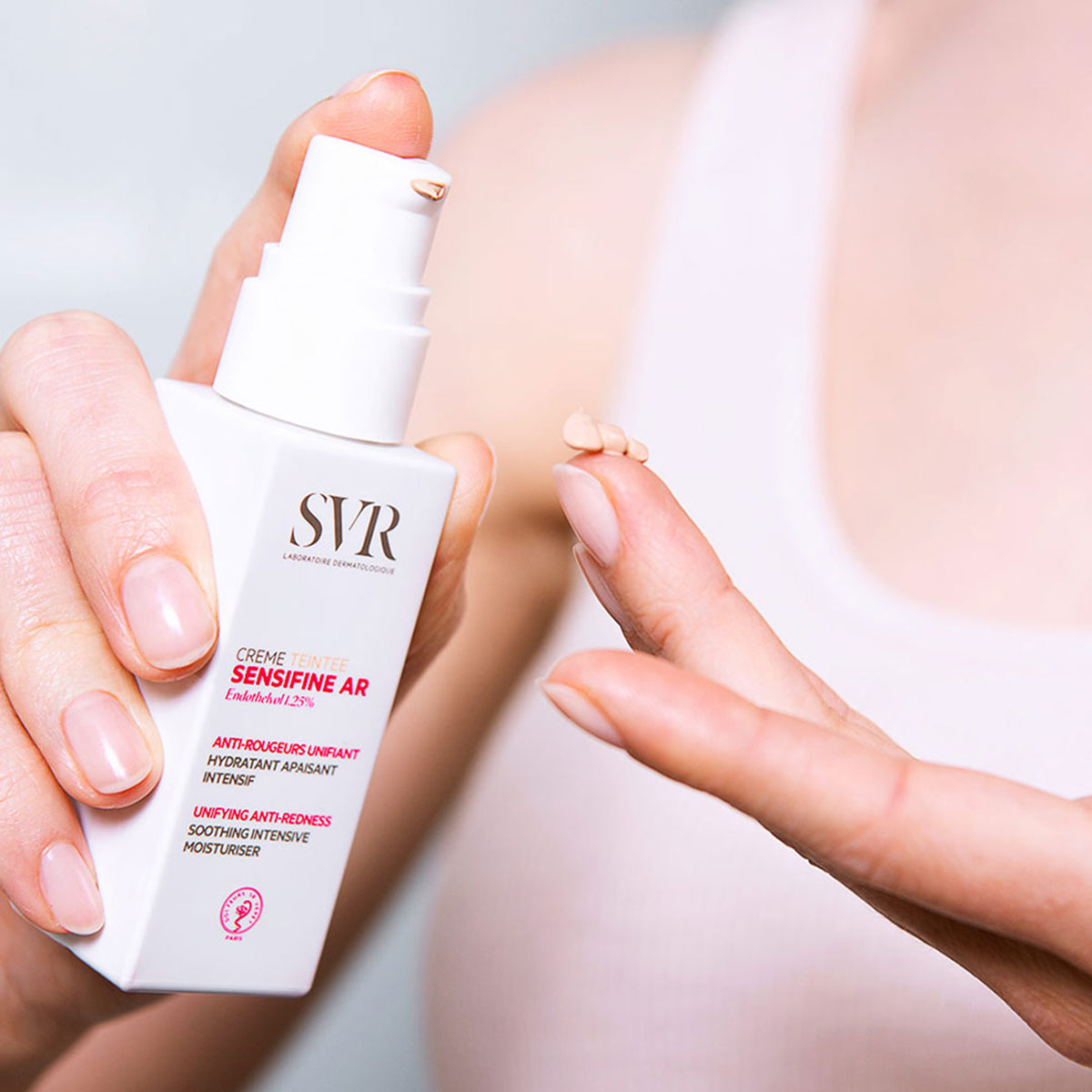 Envase blanco de SVR Sensifine AR Crème Teintée con dosificador, mostrando una gota de crema con color sobre un dedo.
