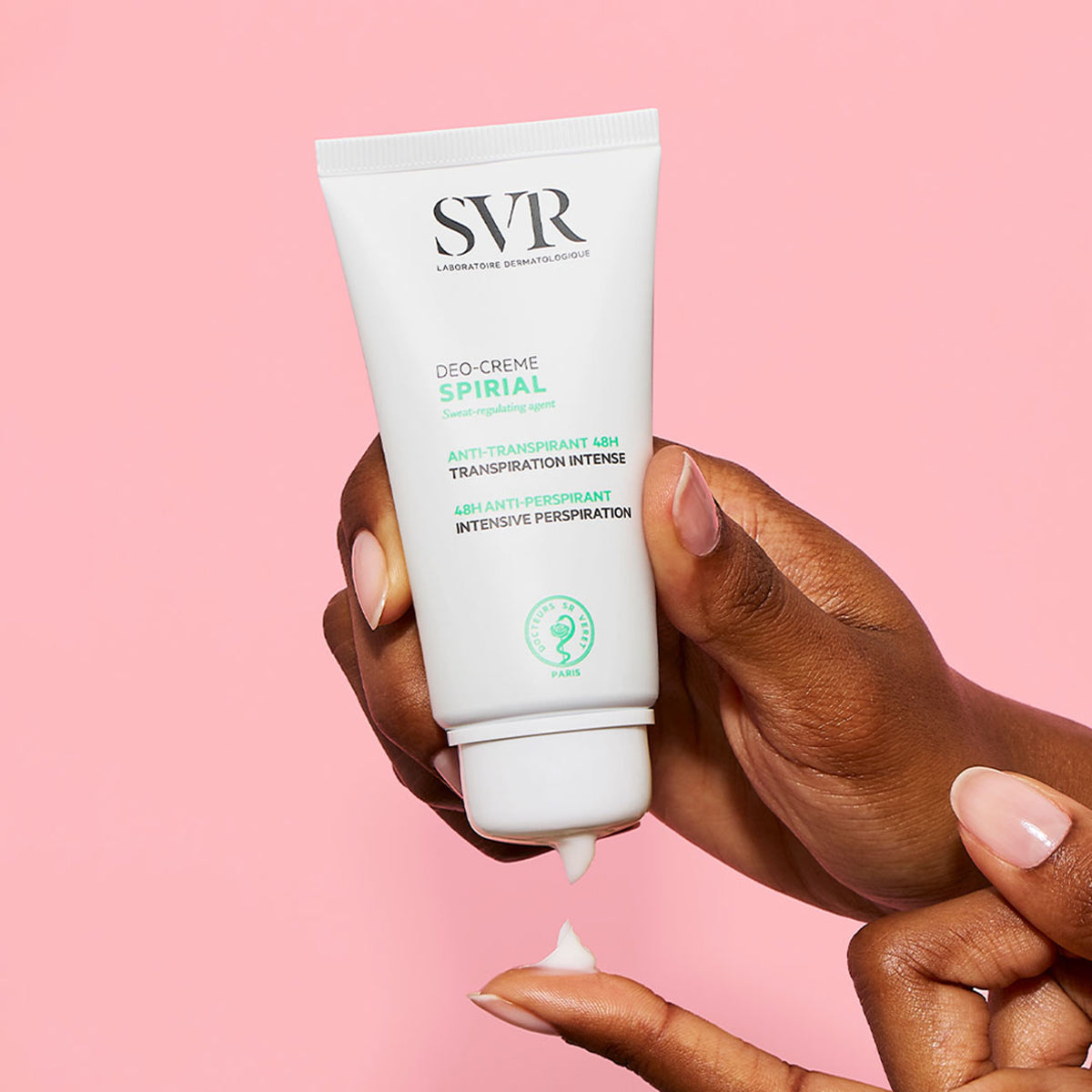 Tubo blanco de crema antitranspirante SVR Spirial siendo aplicado sobre un dedo contra un fondo rosa suave.