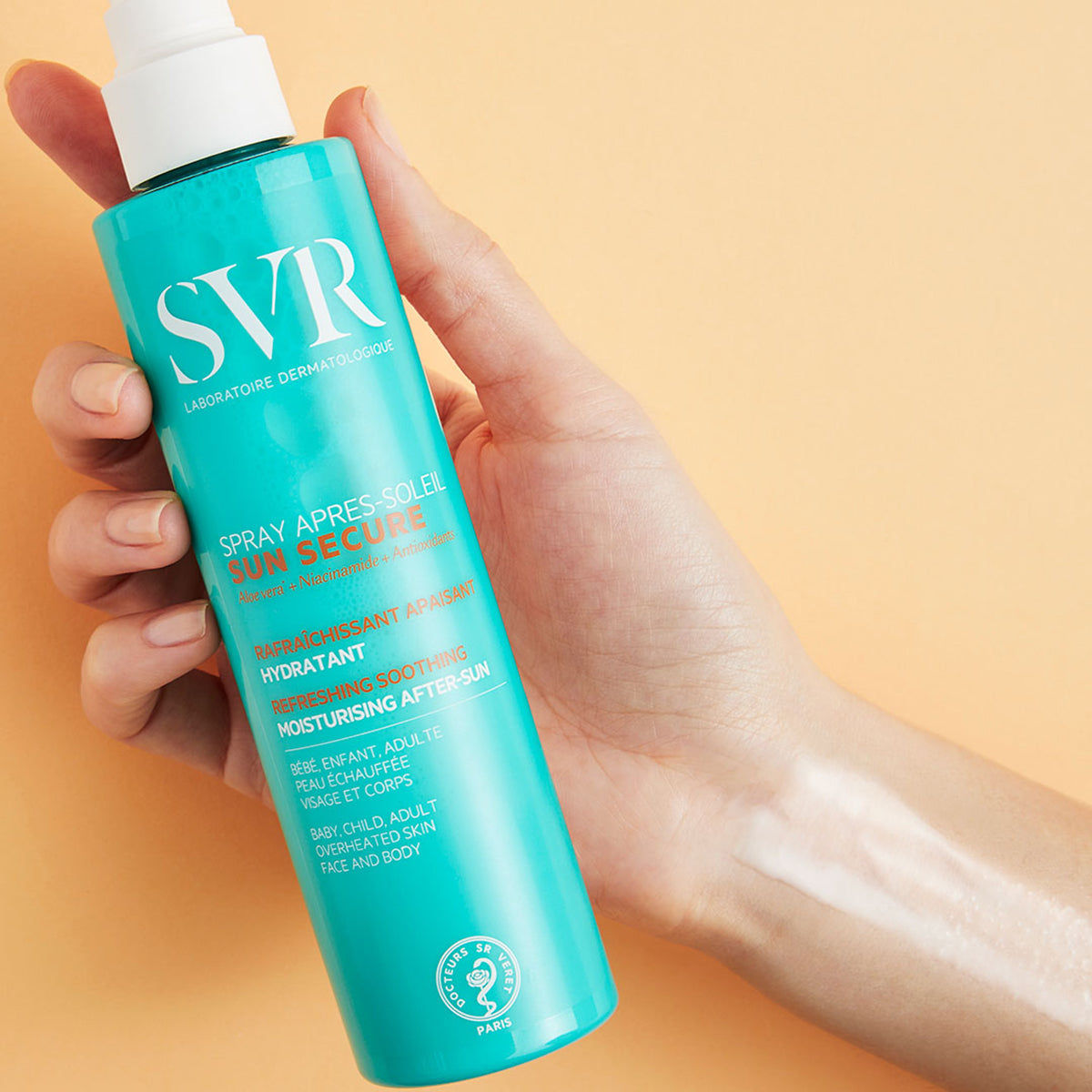 Spray SVR SUN SECURE Après-Soleil en envase turquesa sostenido en una mano sobre fondo naranja suave.