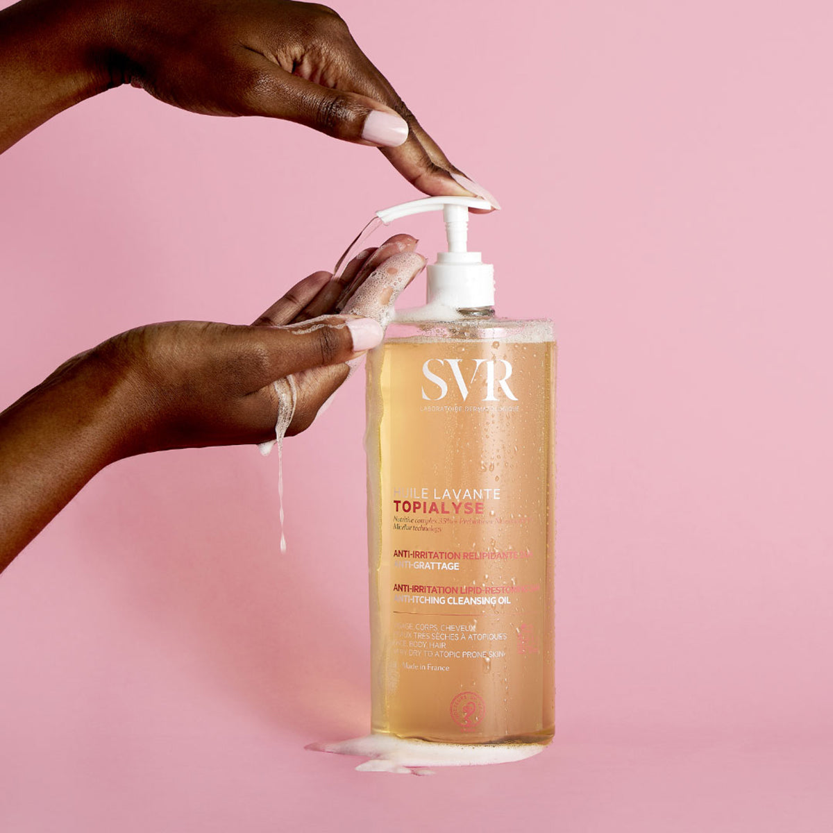 Botella de aceite limpiador SVR Topialyse con dosificador, siendo aplicada en manos sobre un fondo rosa suave.