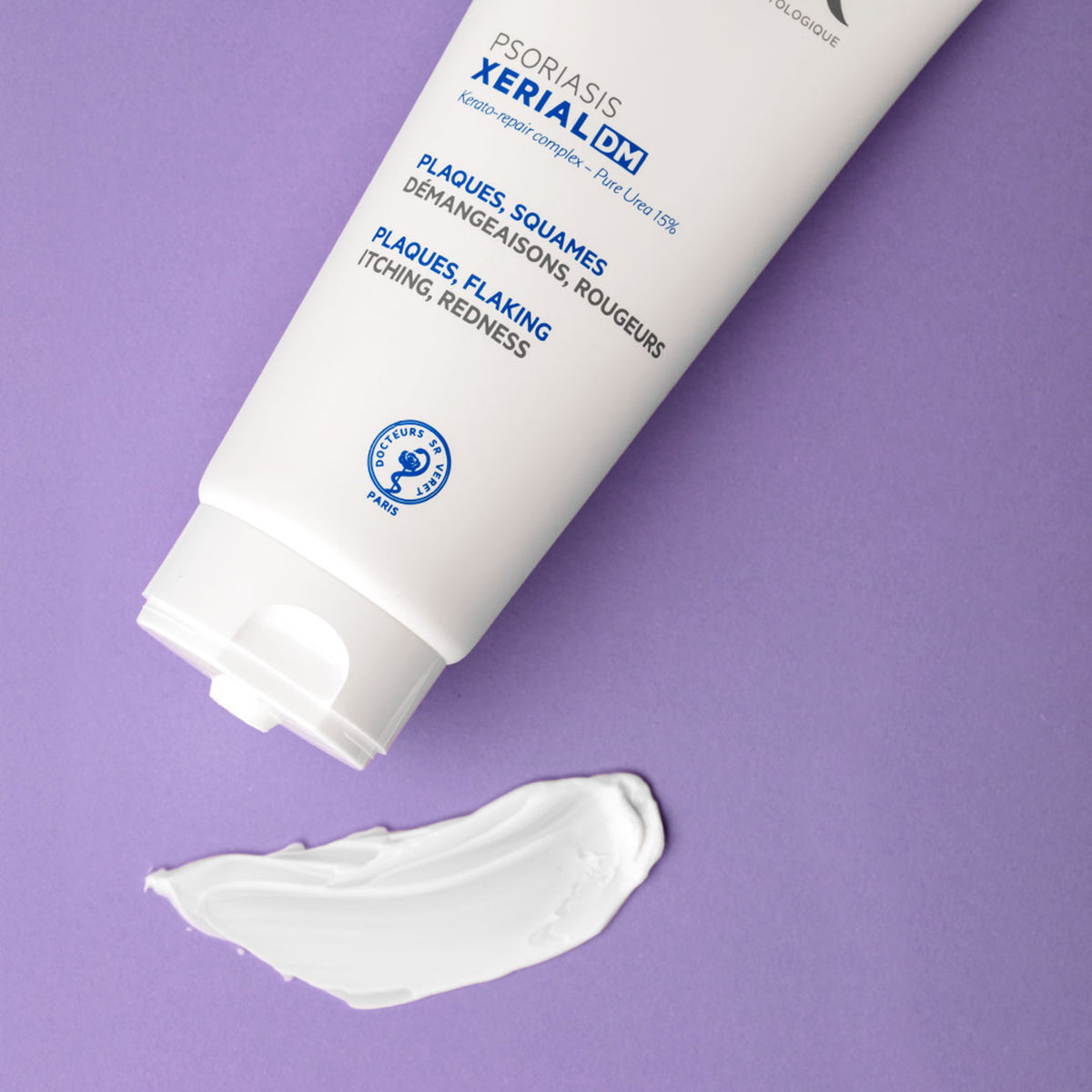 Tubo blanco de crema SVR XERIAL DM para psoriasis con una muestra de textura sobre fondo morado.