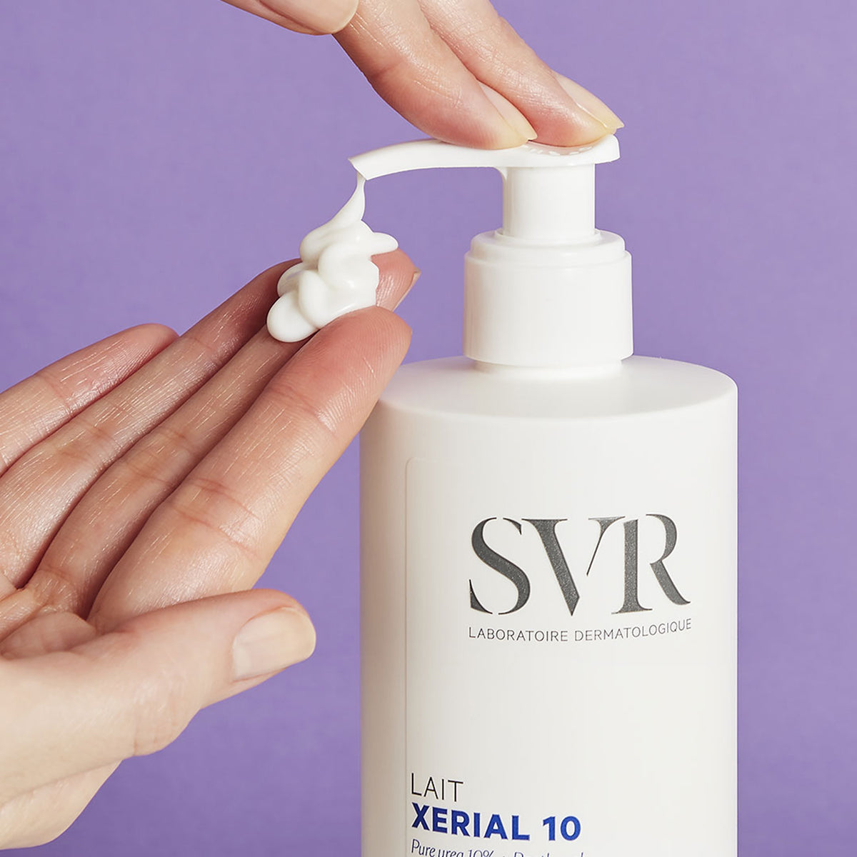 Loción corporal SVR XERIAL 10 en envase blanco con dosificador, aplicando crema blanca sobre una mano contra fondo morado.