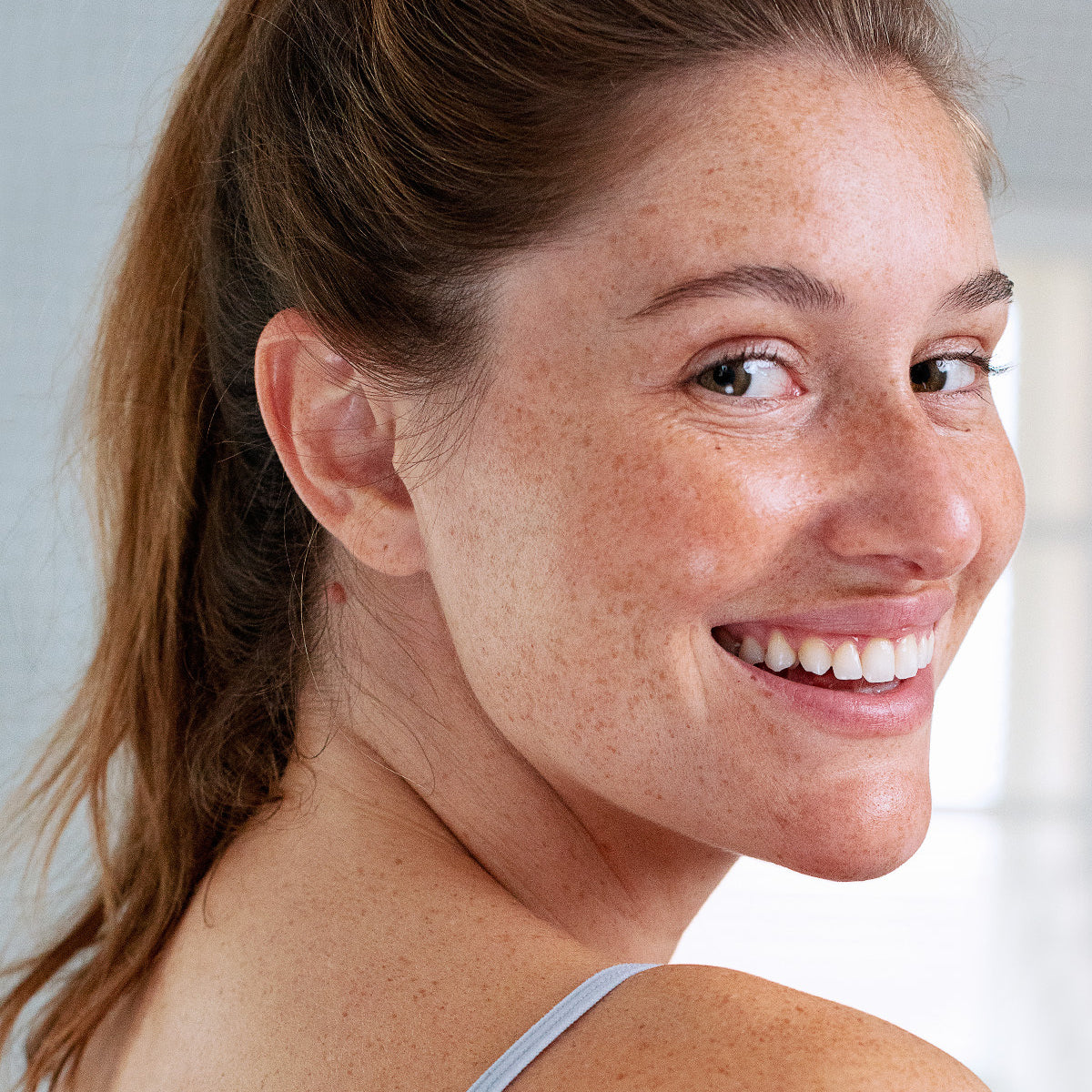 Mujer joven sonriente con pecas y labios hidratados y saludables, mostrando una piel radiante y cuidada.
