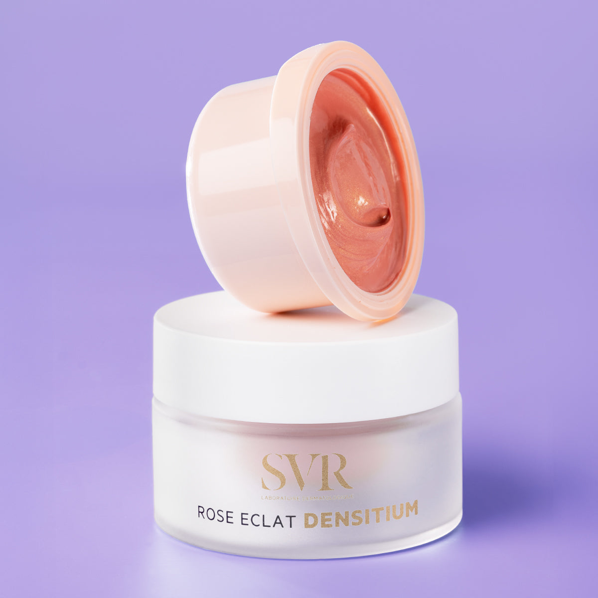 Tarro de crema antiedad SVR Densitium Rose Eclat con tapa abierta mostrando textura rosada sobre fondo morado.