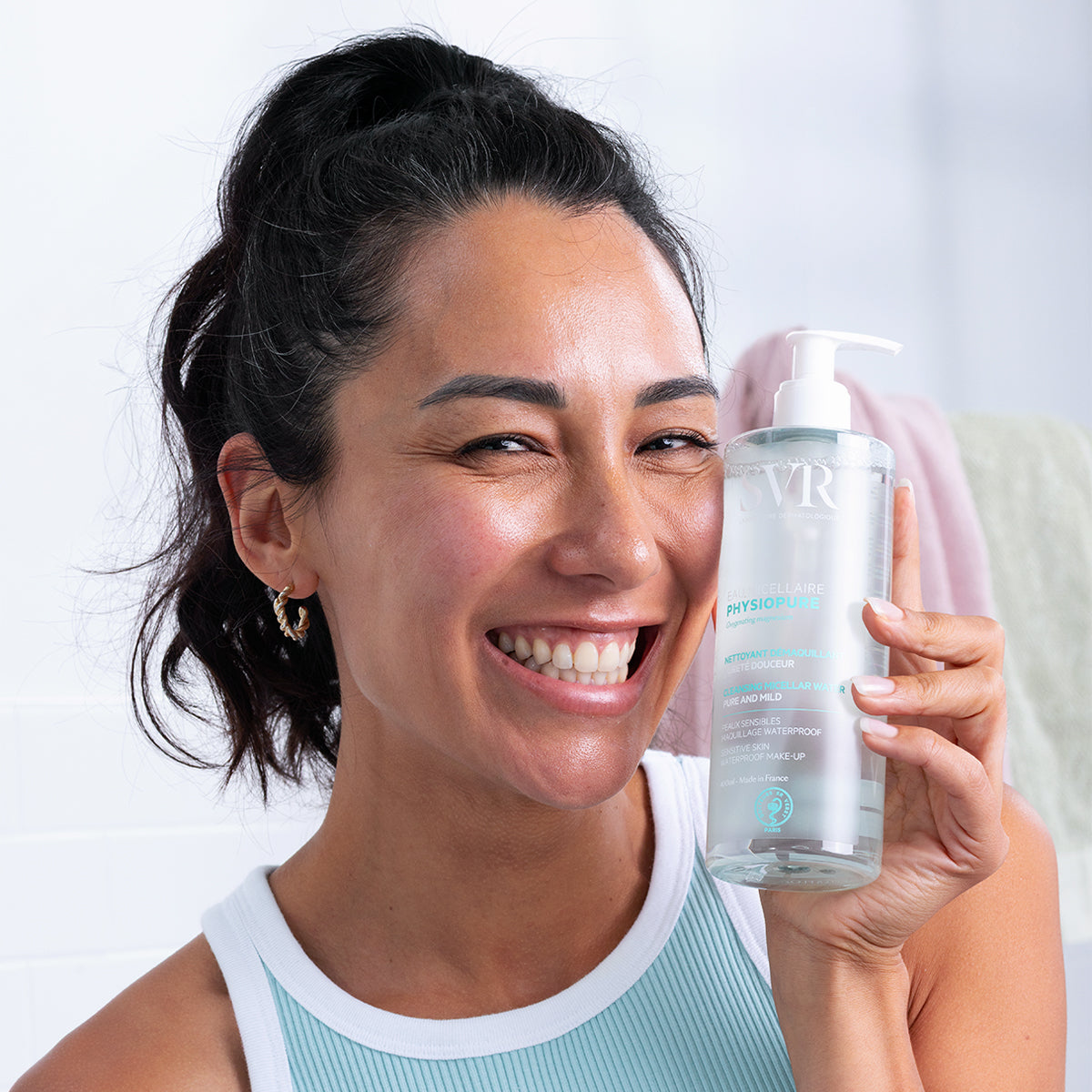 Mujer sonriente sosteniendo un frasco transparente con dosificador de agua micelar SVR PHYSIOPURE para pieles sensibles.