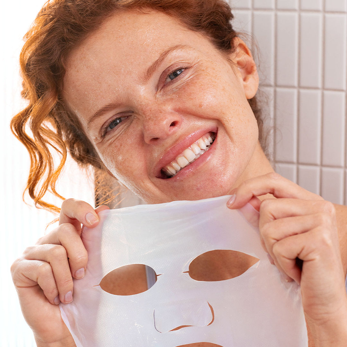 Mujer sonriente sosteniendo una mascarilla facial de biocelulosa transparente y flexible para hidratación intensiva.