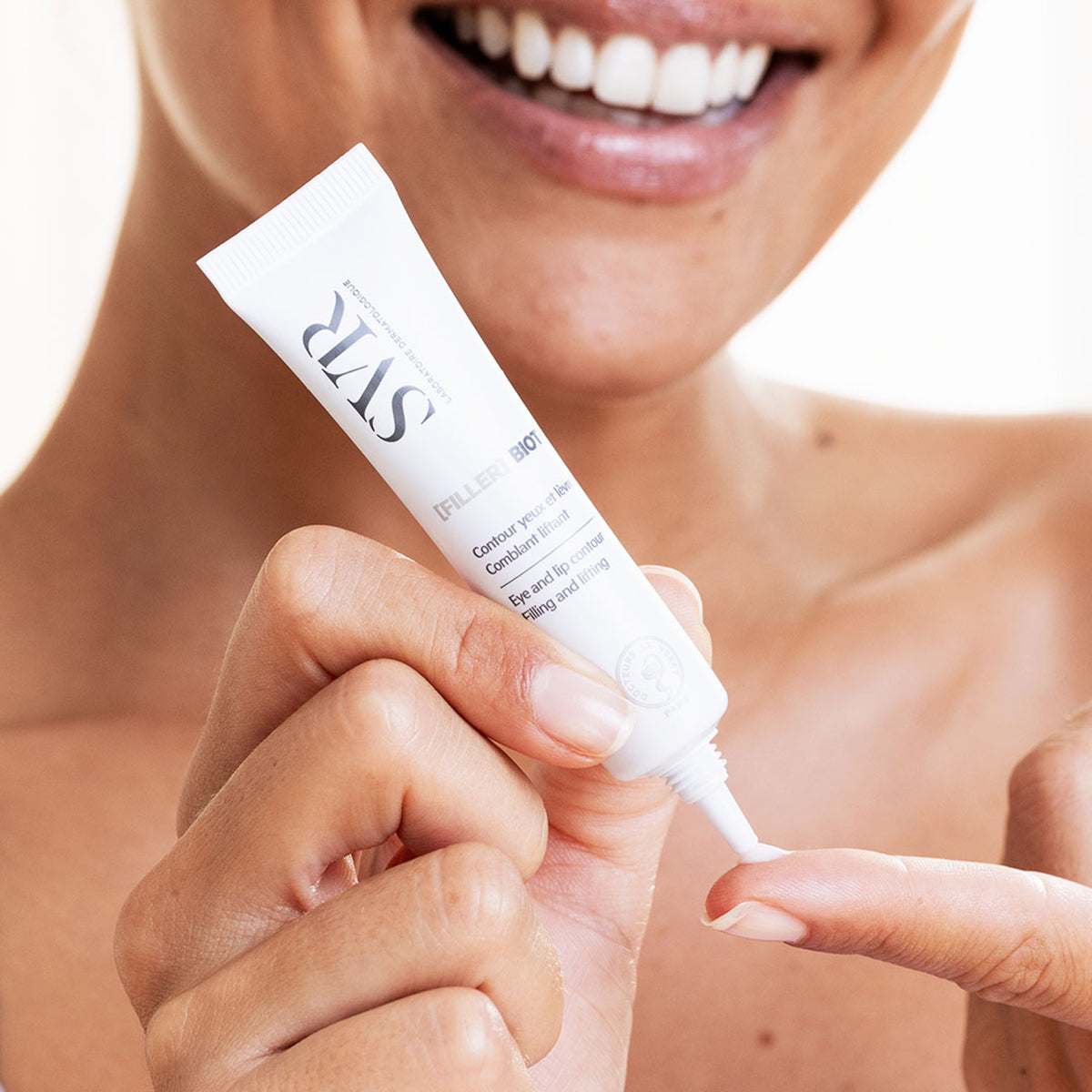 Tubo blanco de 15ml SVR [FILLER] Biotic para contorno de ojos y labios siendo aplicado sobre un dedo.