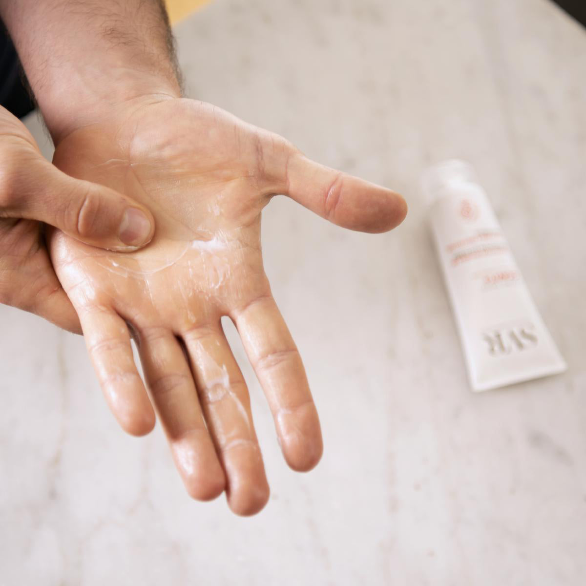 Crema de manos reparadora Cicavit+ SVR aplicada sobre la palma de la mano con un tubo blanco de fondo.