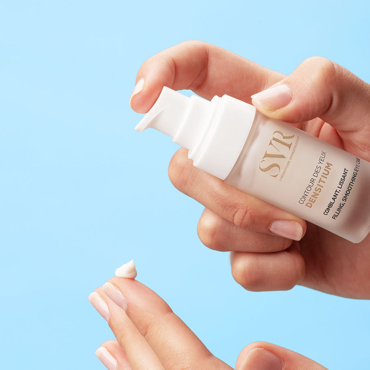 Mano aplicando crema SVR DENSITIUM Contour des Yeux desde un envase dosificador blanco sobre un fondo azul claro.