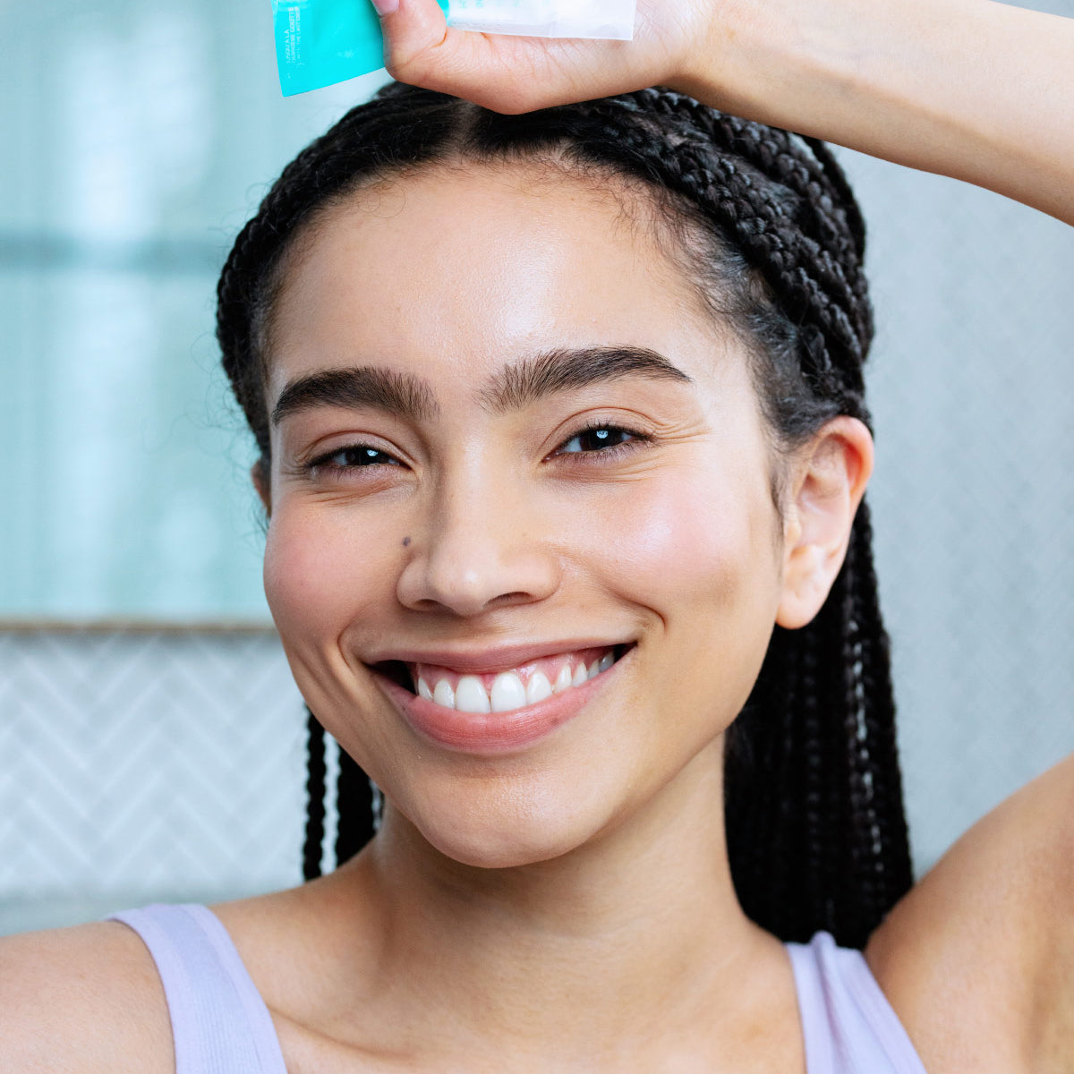 Mujer sonriente sosteniendo un tubo de crema hidratante Hydraliane Riche de color turquesa sobre su cabeza.